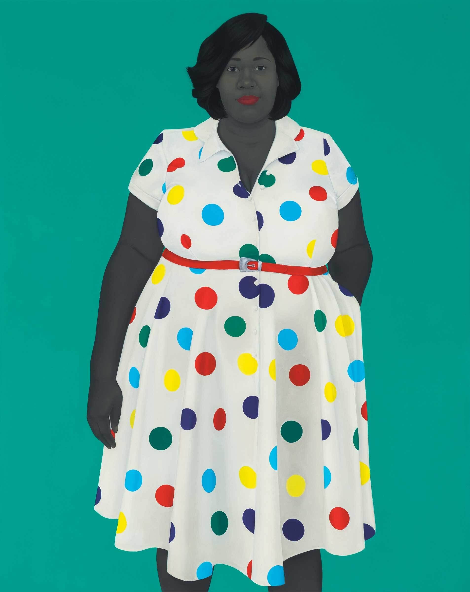 Woman in a white dress with colorful polka dots stands against a teal background, wearing red lipstick and a red belt.