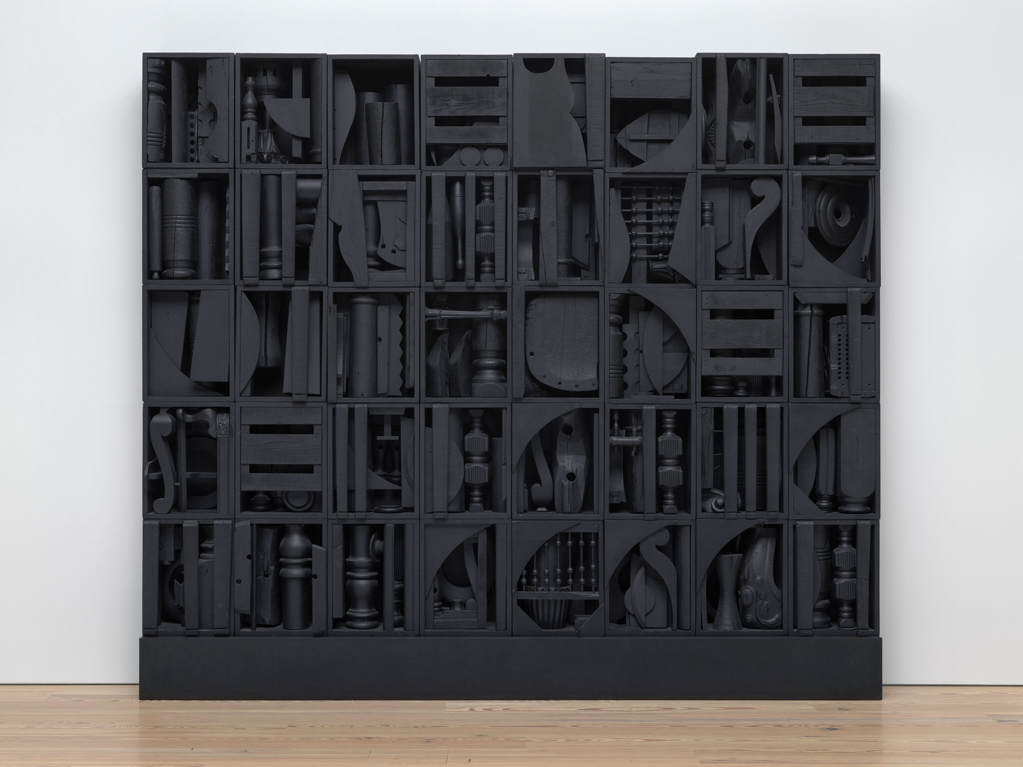 Large black wooden cabinet with many square compartments, each filled with various dark, abstract wooden objects and shapes.