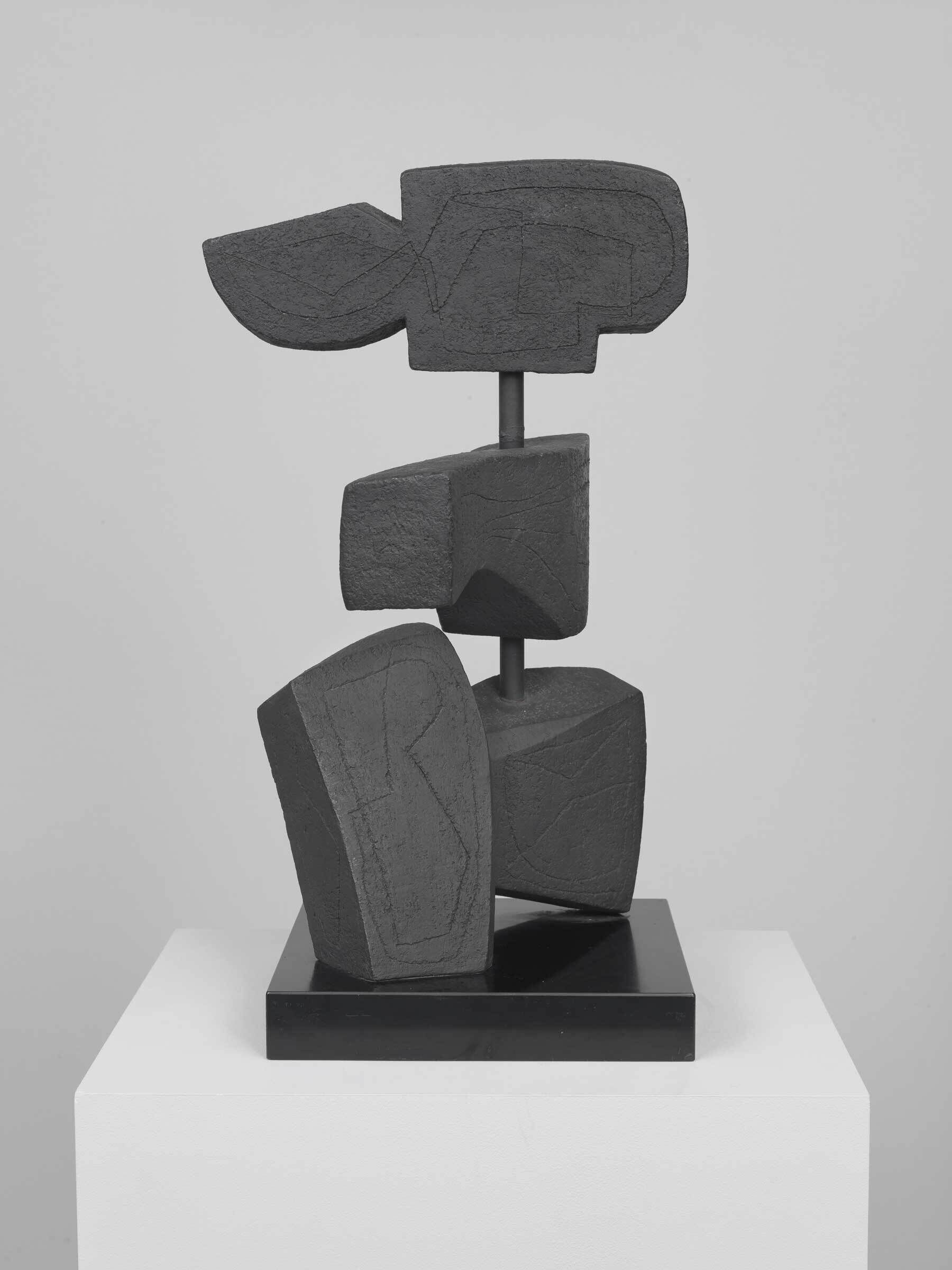 A black abstract sculpture made of three stacked geometric shapes on a black base, displayed on a white pedestal.