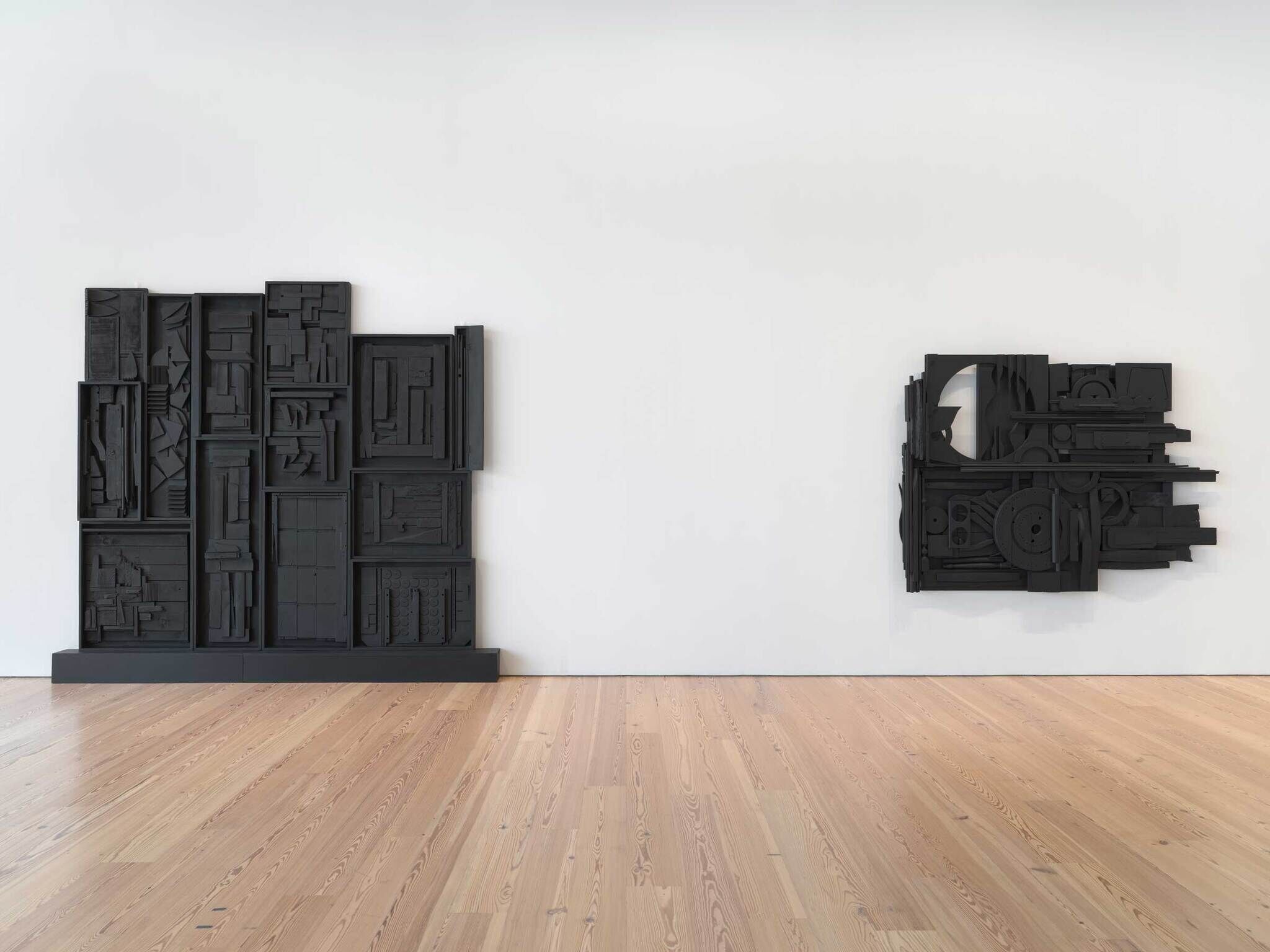 Two big black sculptures against a white wall made out of found objects.