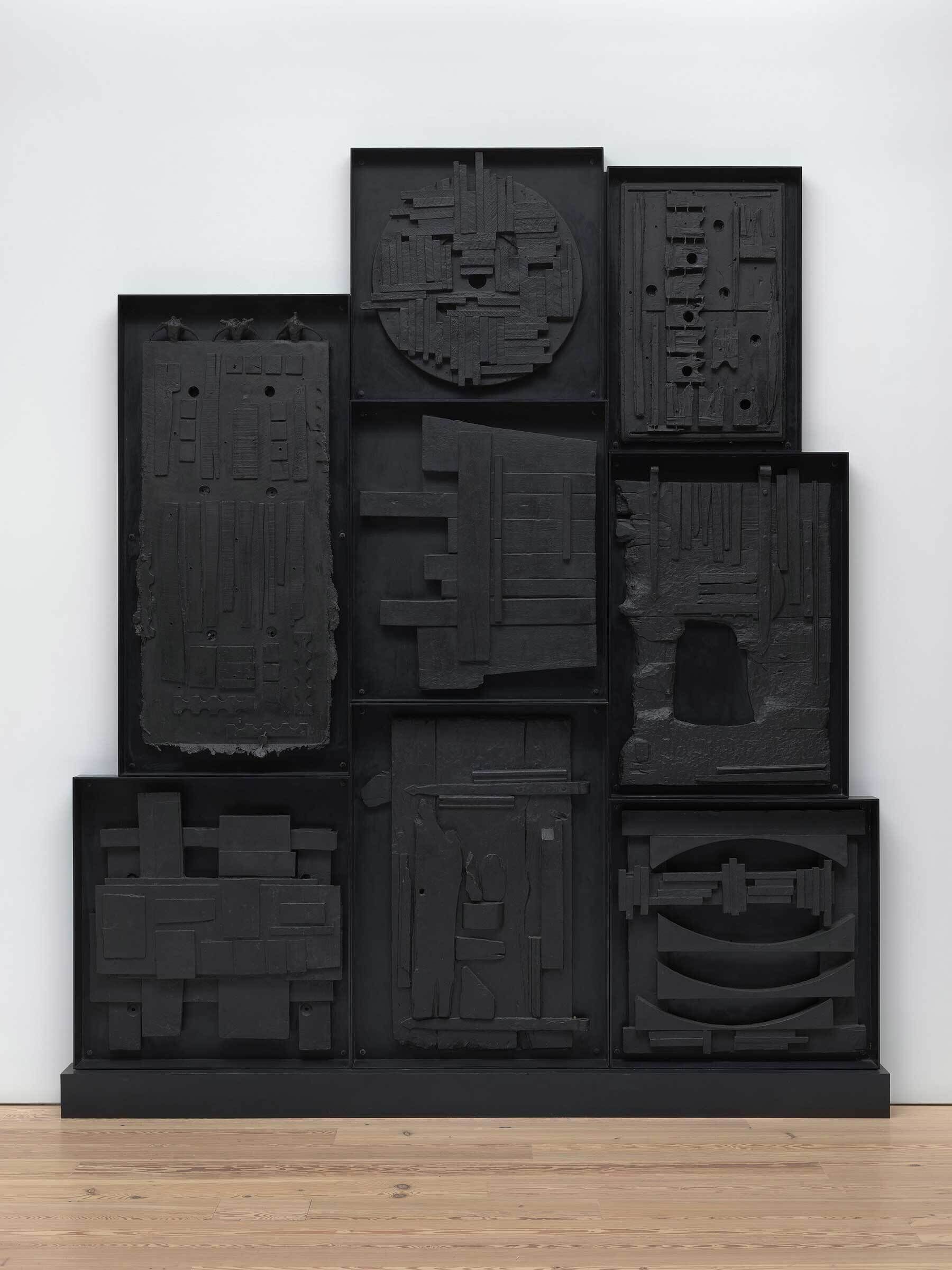 Large black wall sculpture made of nine textured panels with geometric and abstract shapes arranged in a grid.