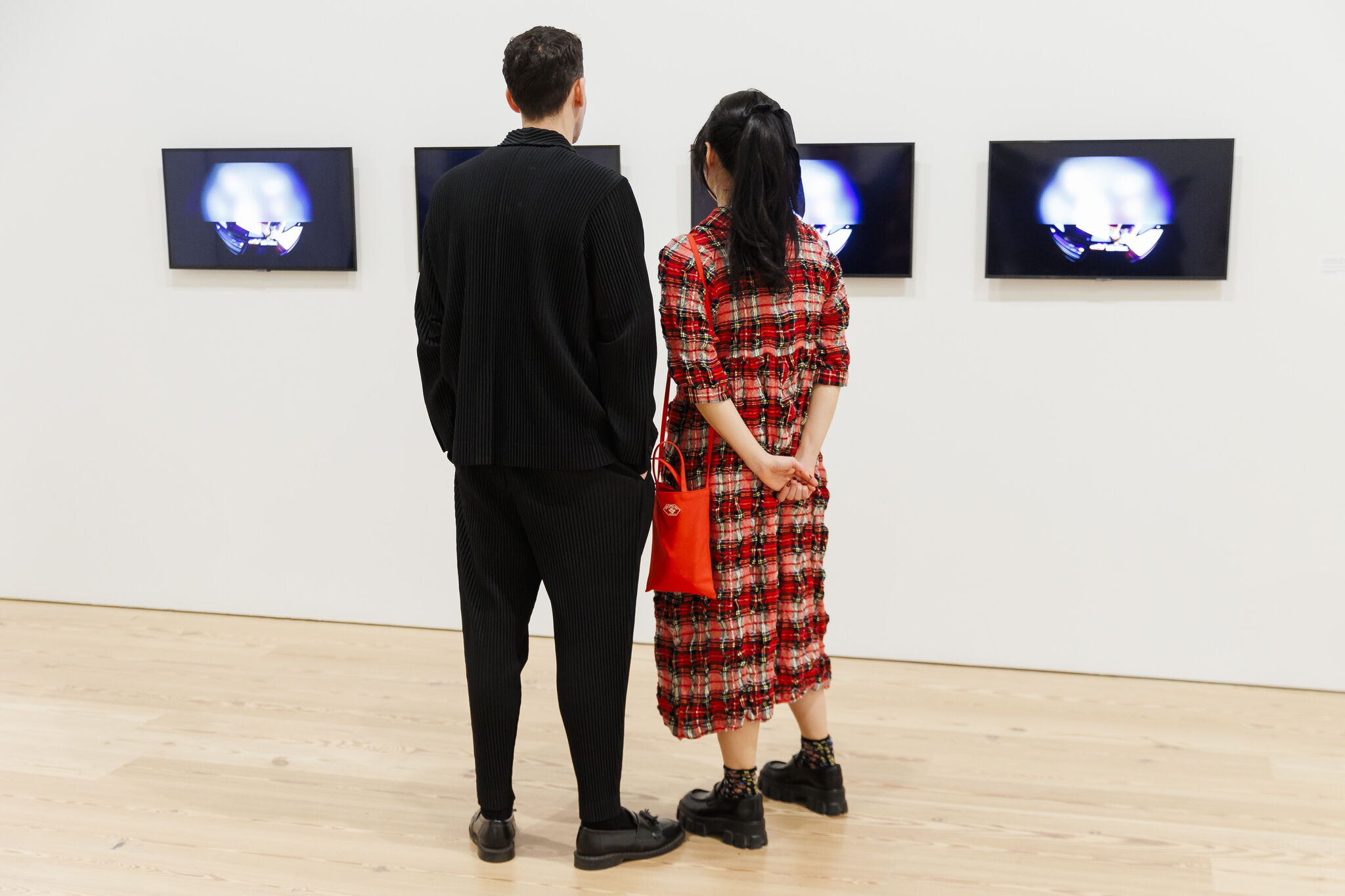 Two people stand side by side in front of three screens displaying abstract images in an art gallery.