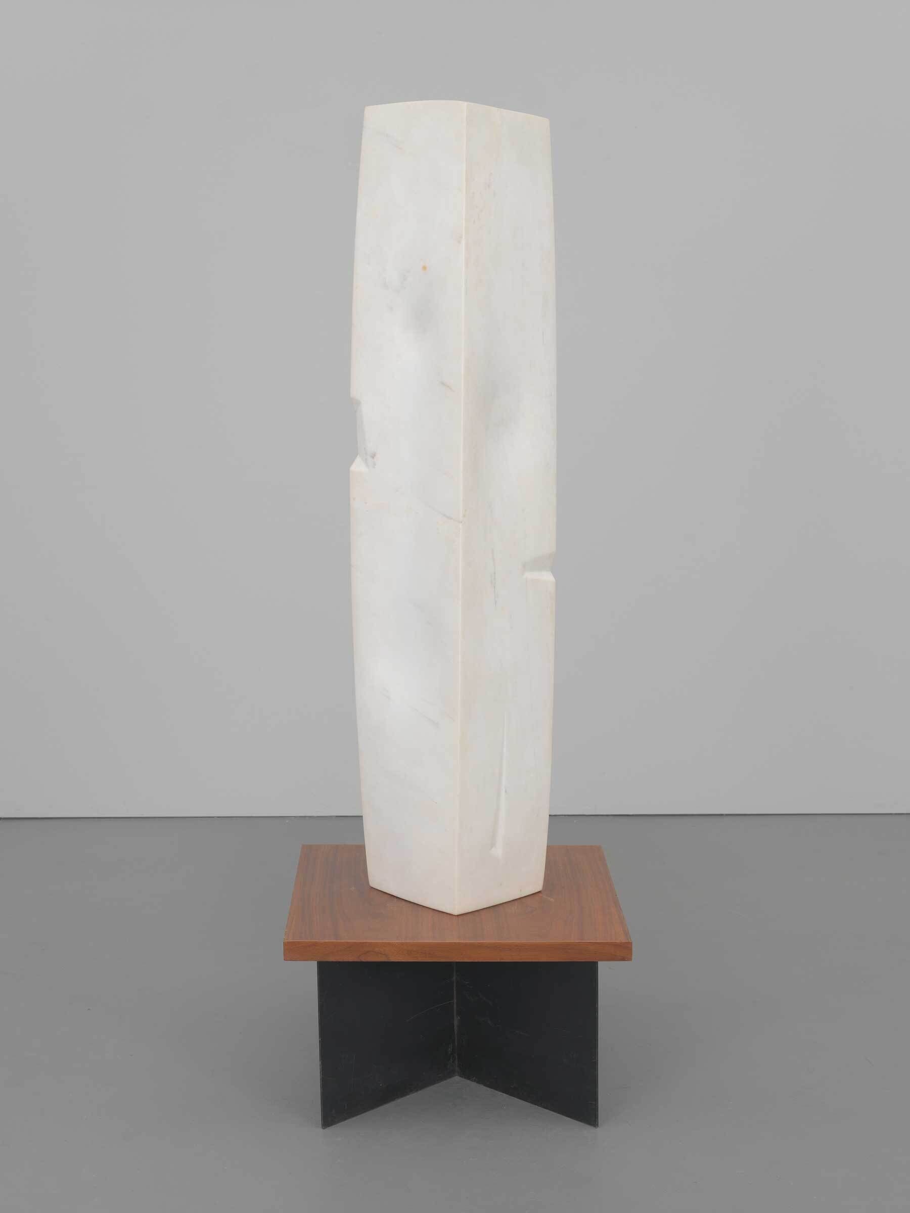 Tall, smooth white stone sculpture with simple geometric shape, standing on a wooden and black base.