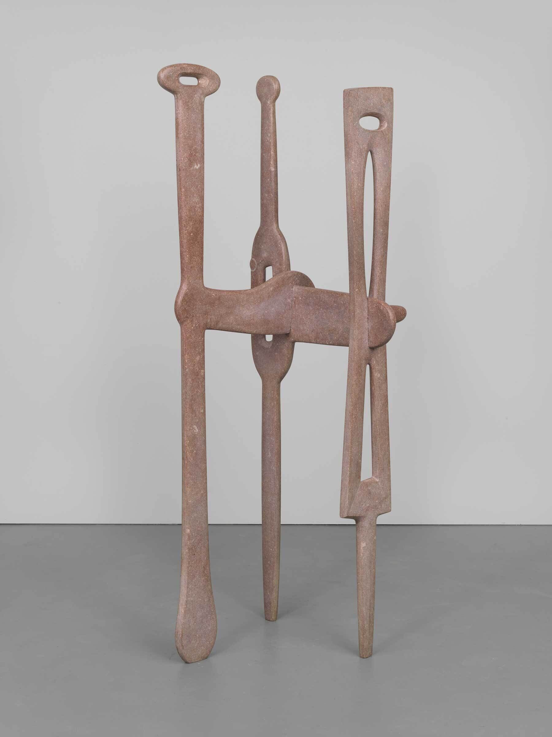Tall abstract sculpture made of reddish-brown material, featuring three elongated, vertical shapes joined together.
