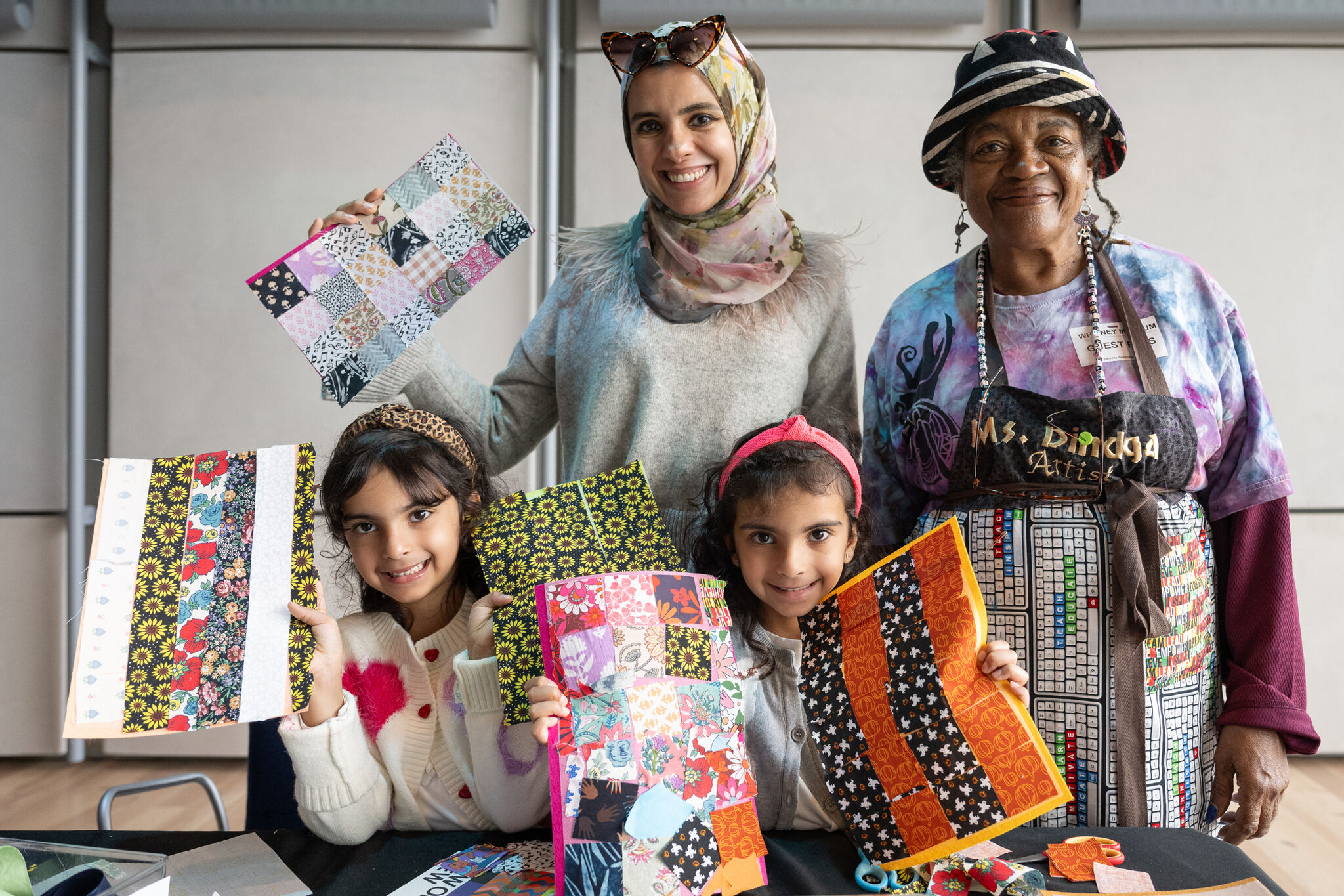 Two women and two girls smile and hold up colorful patchwork art projects.