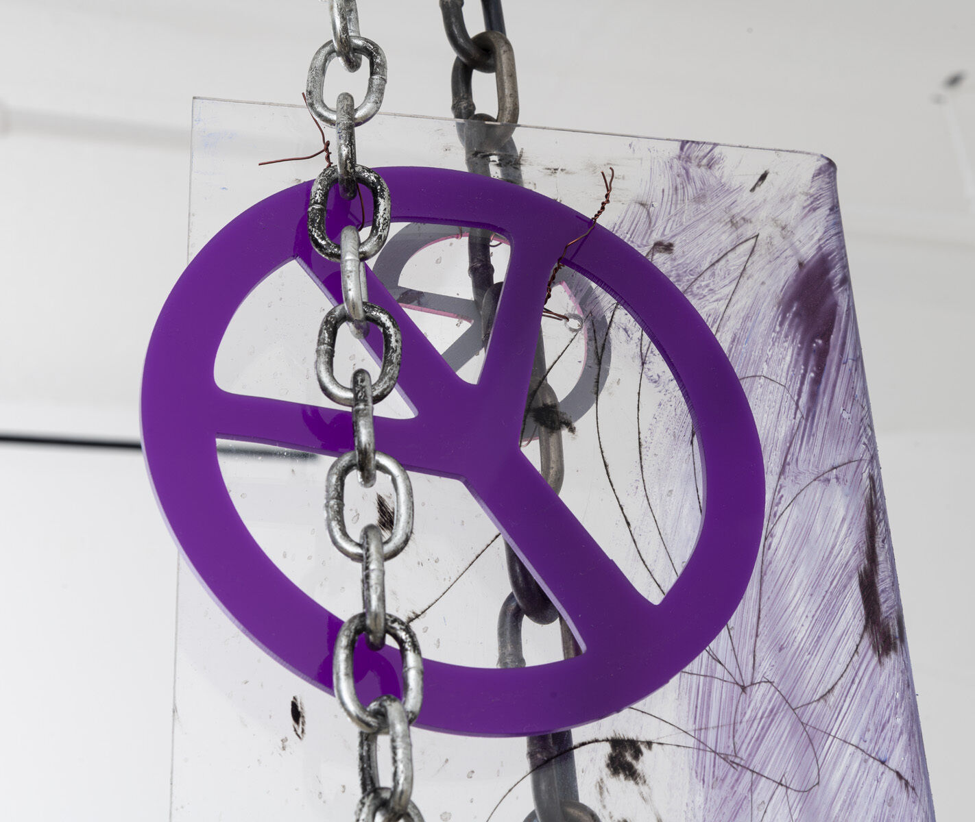 A purple peace sign made of plastic hangs from a metal chain against a white background.