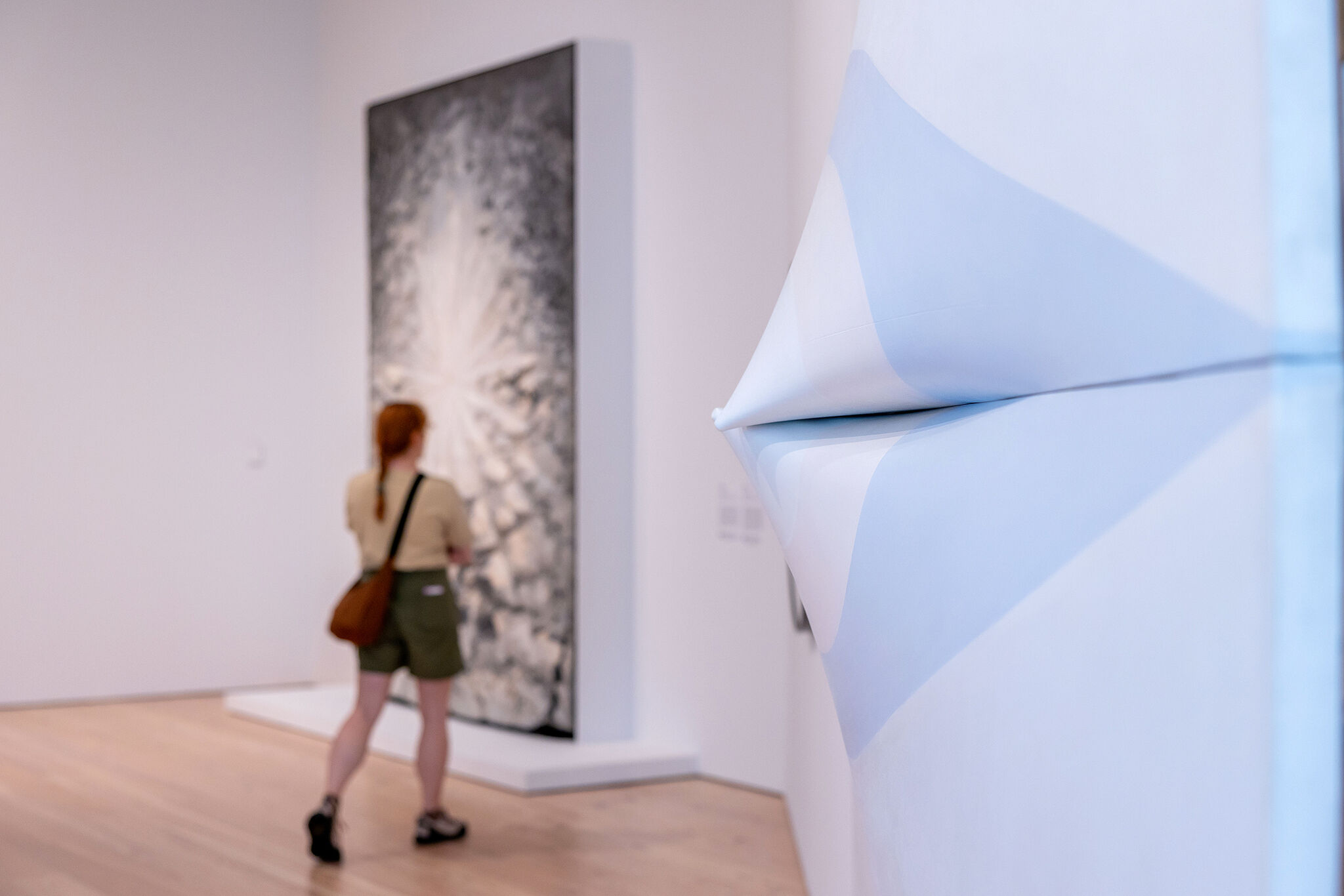 Person with a brown bag looks at abstract art in a modern gallery with a white sculptural piece nearby.