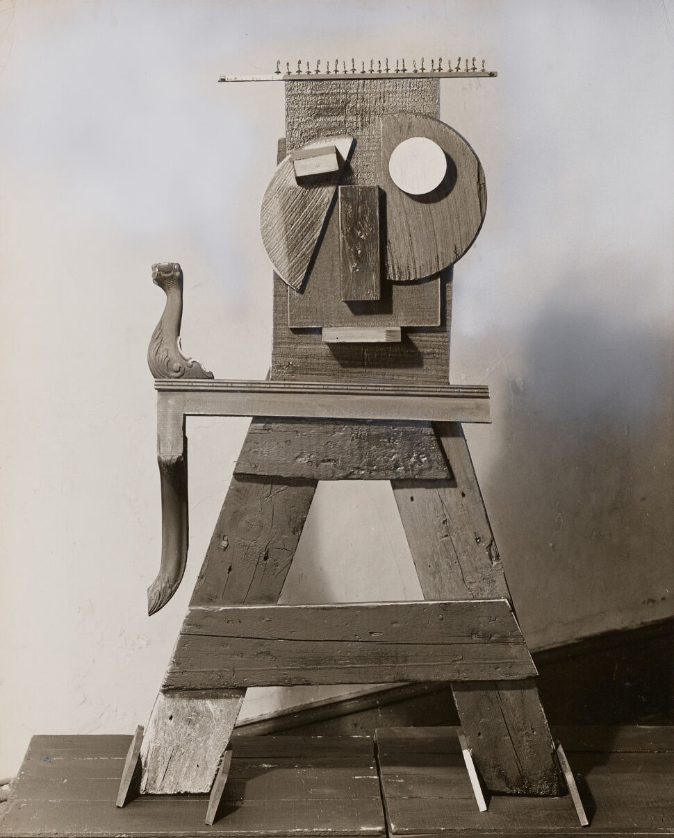 Wooden sculpture arranged to look like a person with a round face and geometric features.