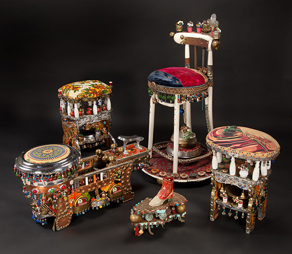 Five colorful, decorated stools and benches with beads, fabric, and small objects attached, arranged against a dark background.