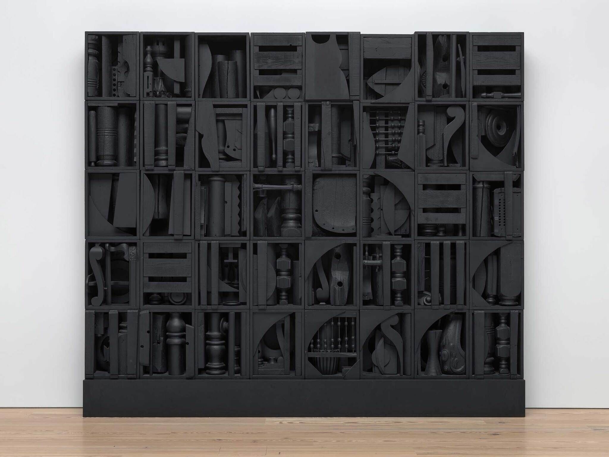 Large black wooden cabinet with many square compartments, each filled with different black-painted wooden objects and shapes.