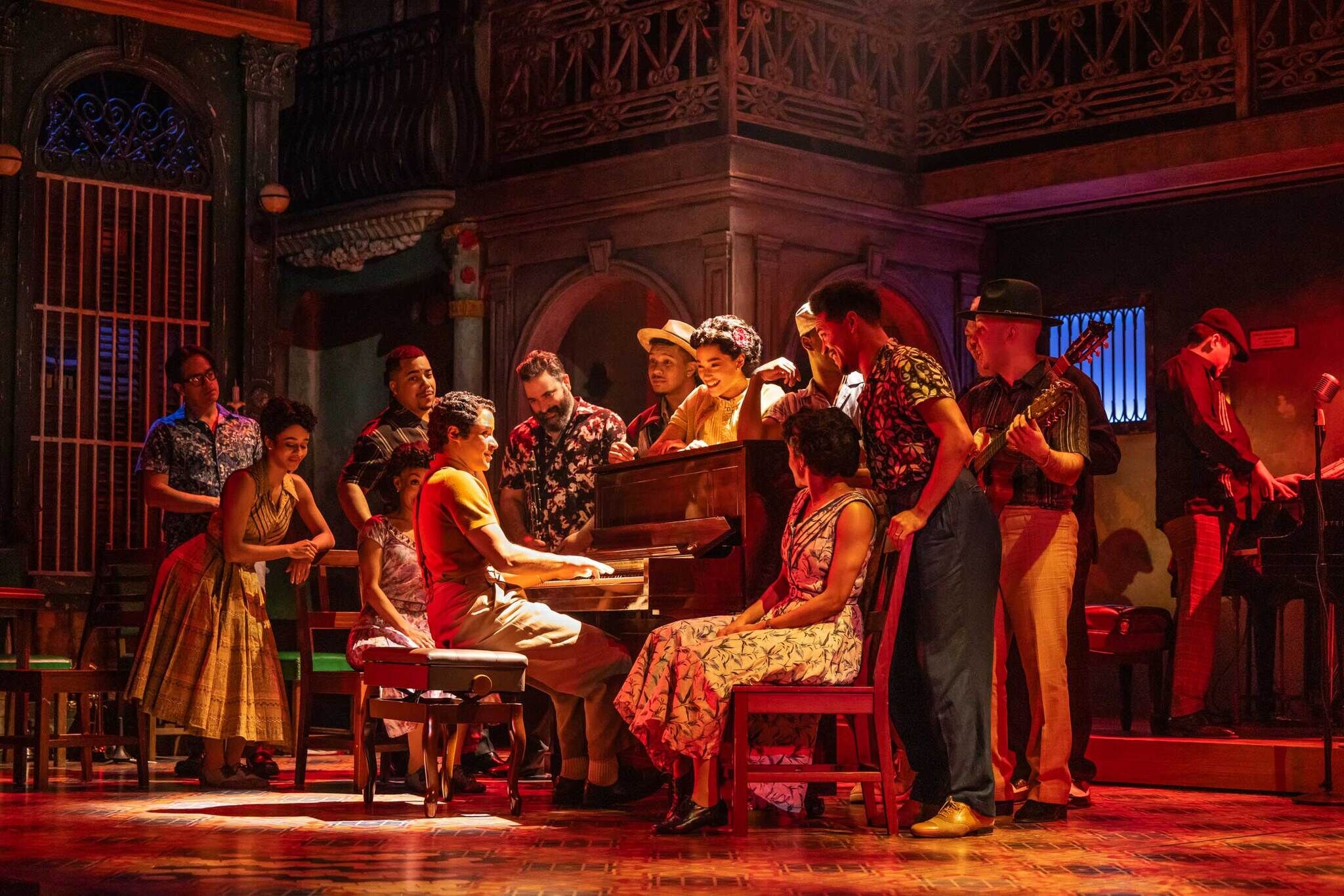 A group of people onstage gathered around an upright piano, where one person is playing.