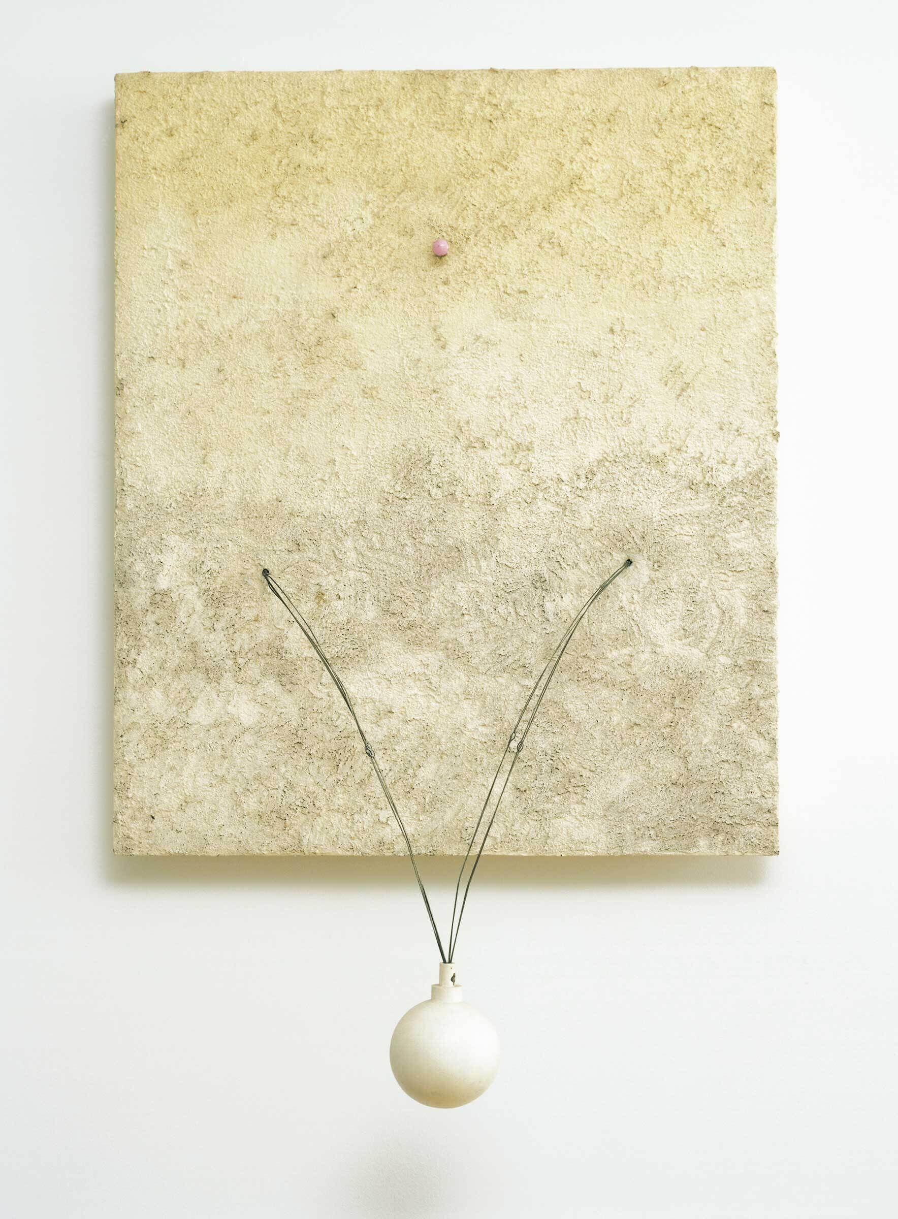 A textured beige square panel with a small pink dot and a white ball hanging by two wires.