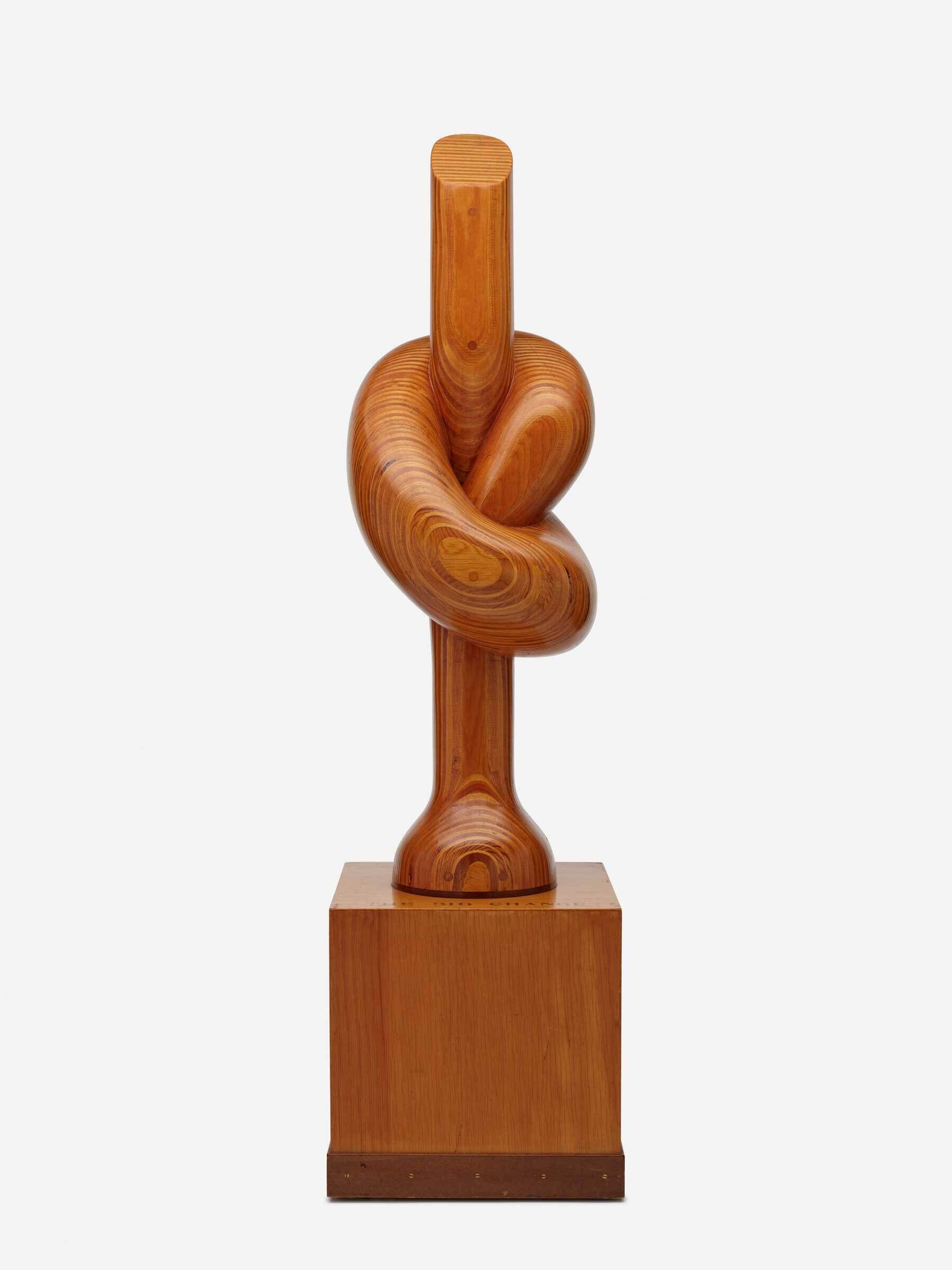 A smooth wooden sculpture shaped like a thick stick tied in a knot, standing on a square base.