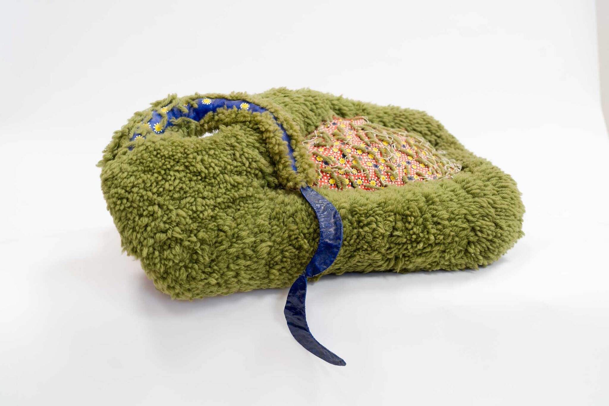 A soft, green, fuzzy object with a blue ribbon and a section of colorful beads and netting.