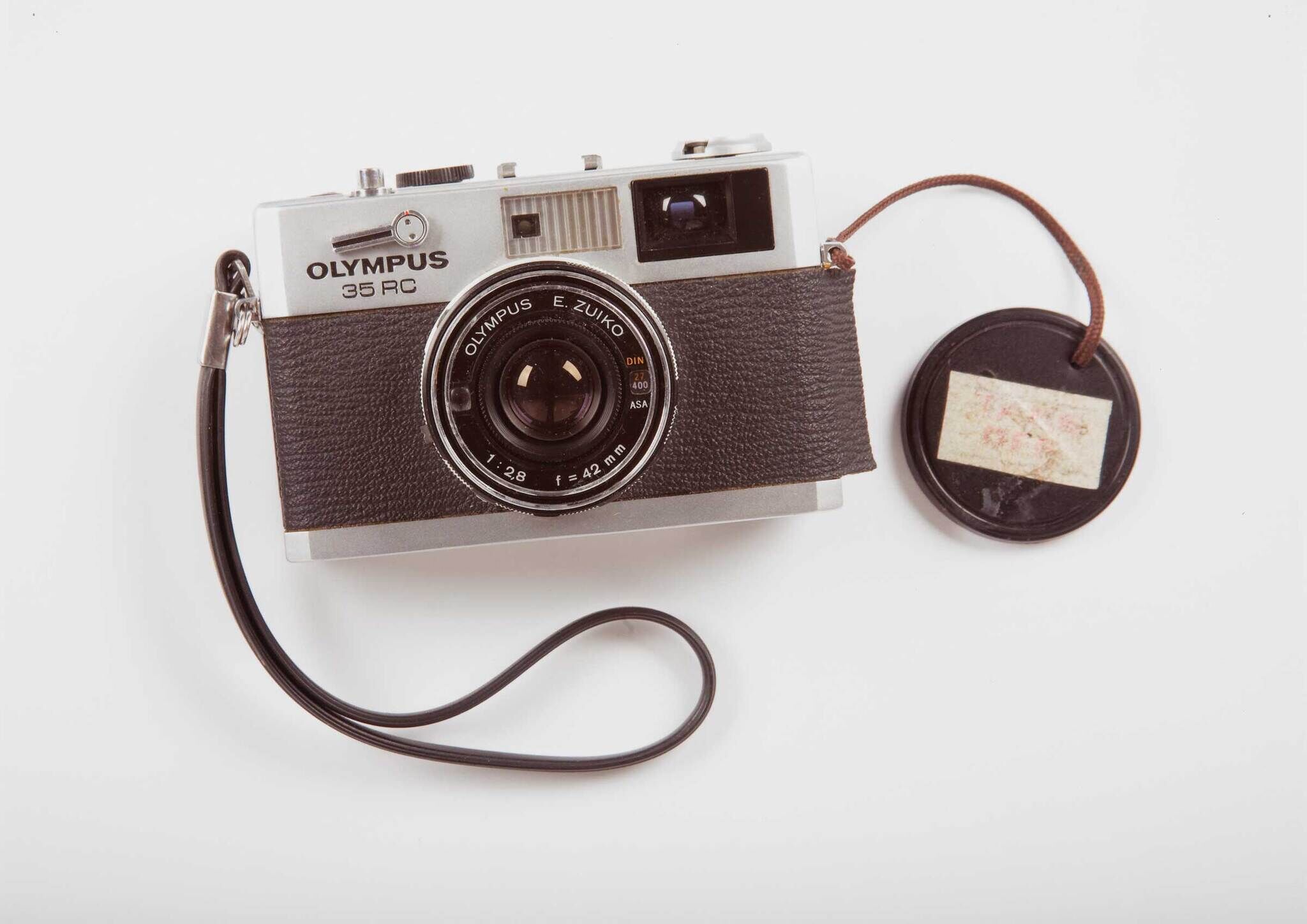 Olympus 35 RC film camera with a wrist strap and a lens cap attached by a string.