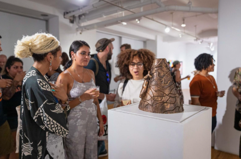People gather around a brown, textured sculpture displayed on a white pedestal in an art gallery.