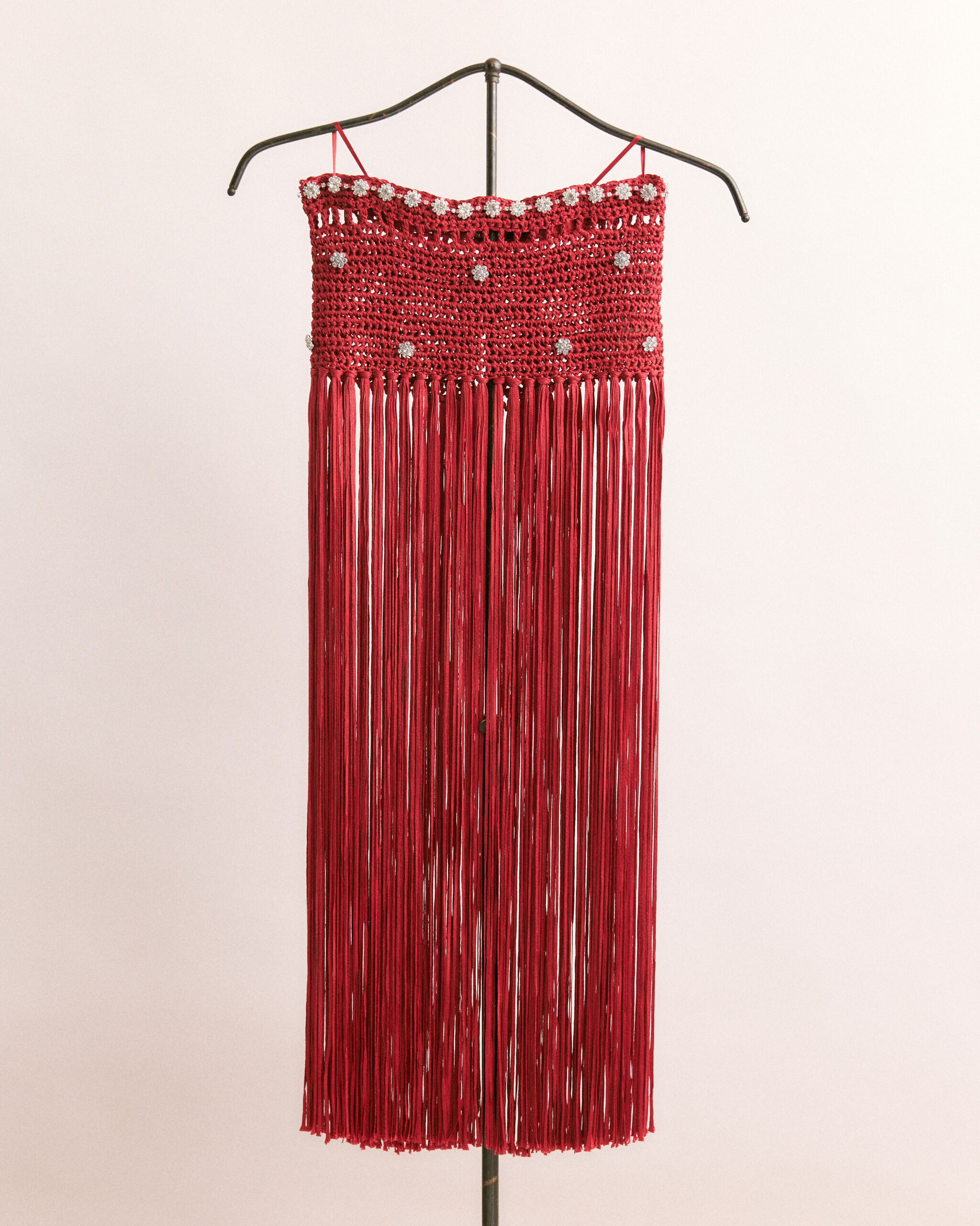 A red crocheted fringe dress with beaded accents hanging on a metal hanger.