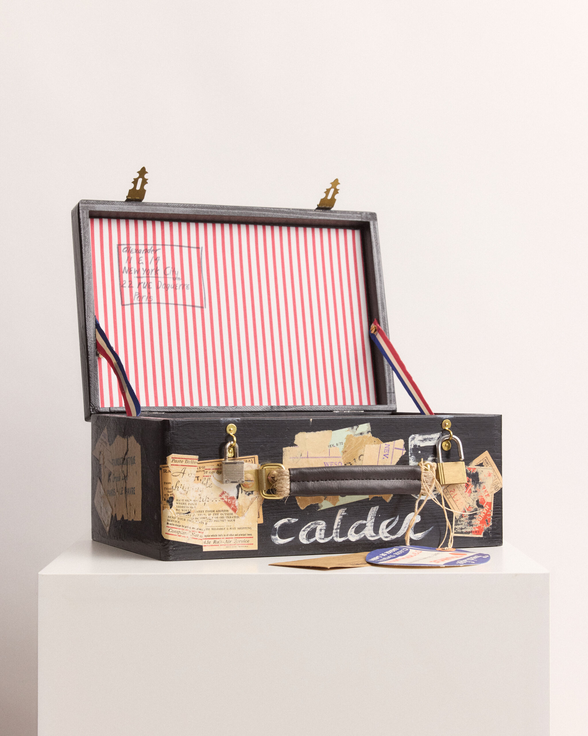 A small black travel trunk with red-striped lining, old travel stickers, and a "calder" name on front.