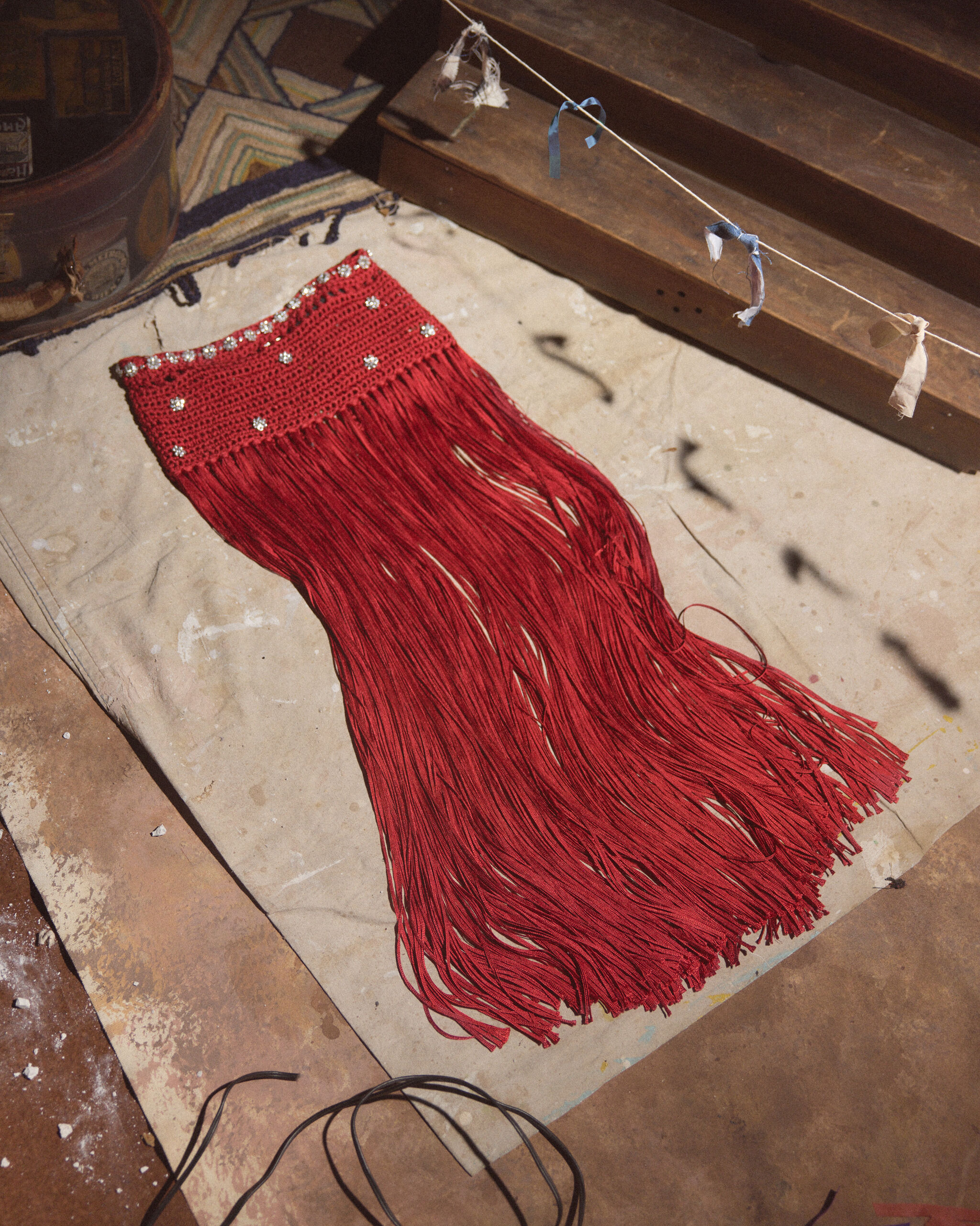 A red crocheted fringe panel with beaded trim lies flat on a workroom floor.