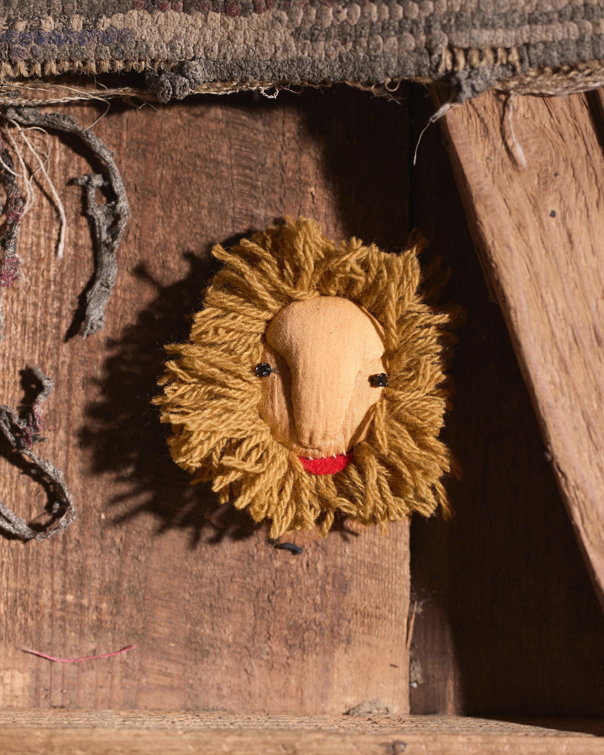 A small handmade lion head puppet with yarn mane and red felt mouth on a wooden board.