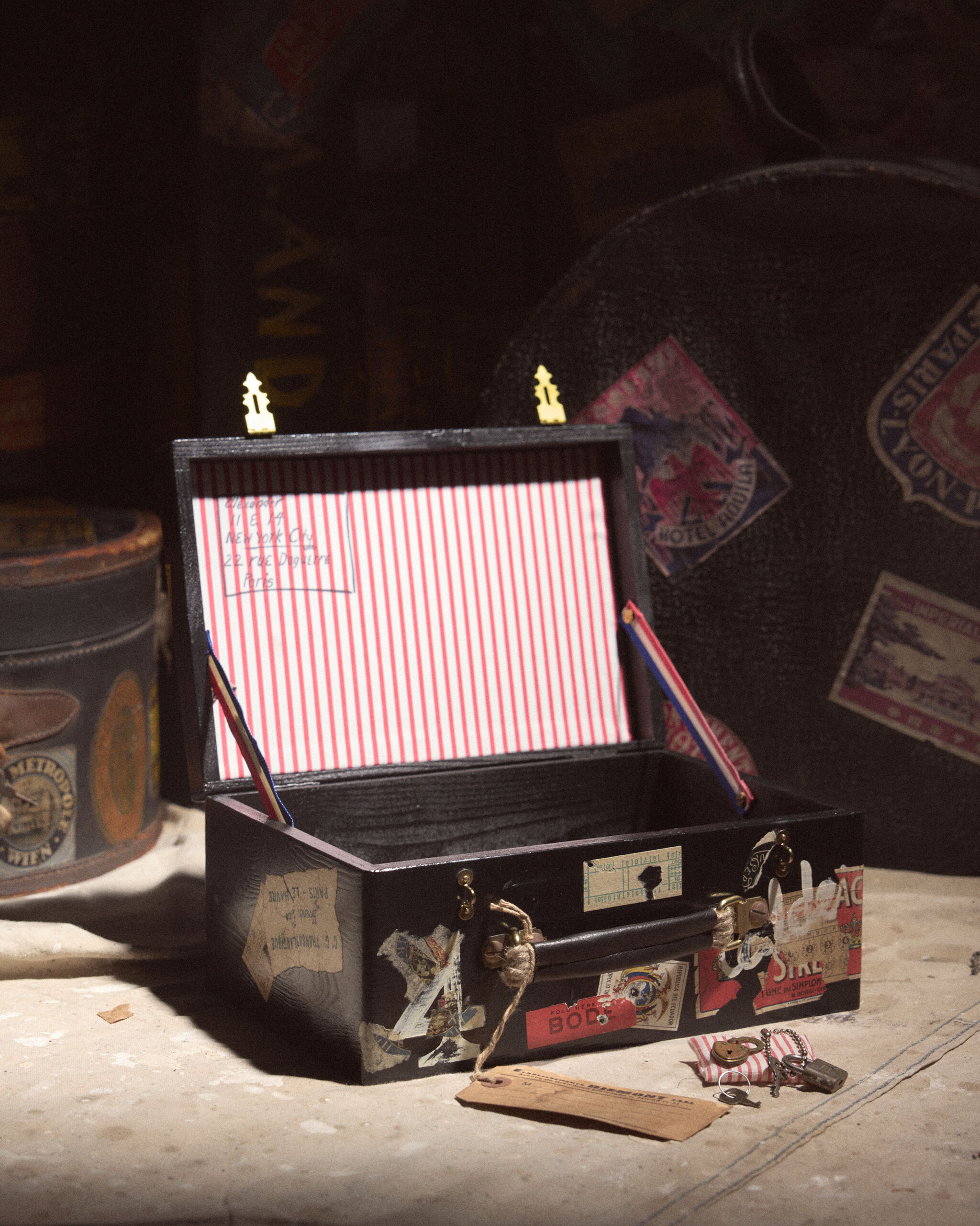 A small open vintage suitcase with red-striped lining and travel stickers sits with keys.