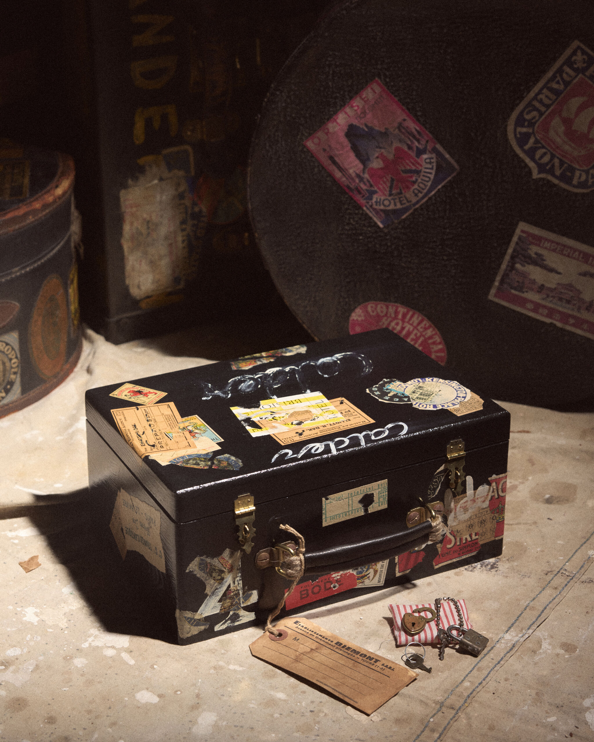 Small black travel case covered in vintage stickers with a worn luggage tag and keys nearby.