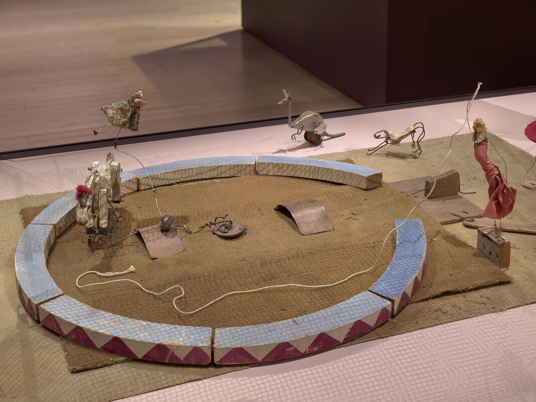 Miniature circus ring with small puppet animals and a red-clad acrobat connected by wires.