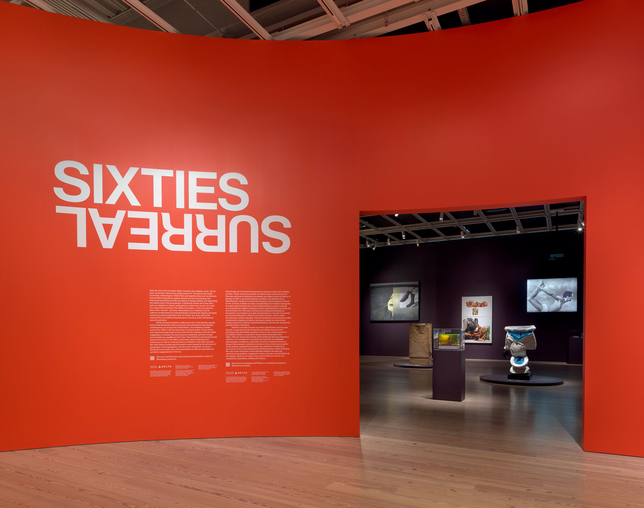 Large red gallery wall with upside-down white title "Sixties Surreal" and entrance to artworks.