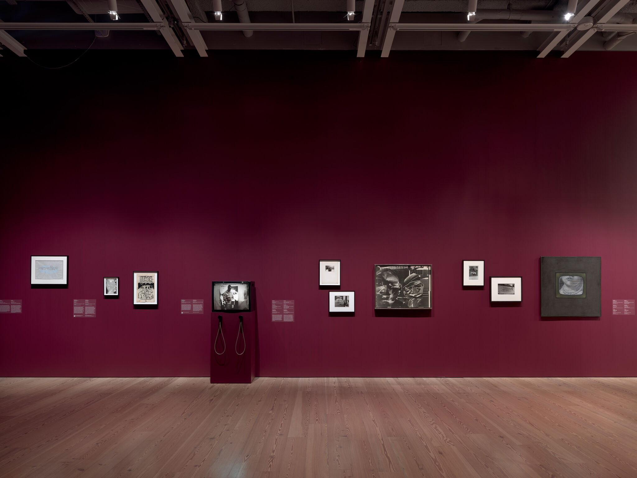 Gallery wall painted deep purple displaying nine framed artworks and a small video monitor with headphones.