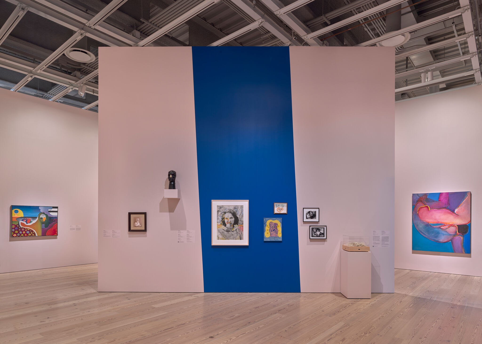 Gallery wall with a central vertical blue stripe featuring several framed paintings and a small sculpture.