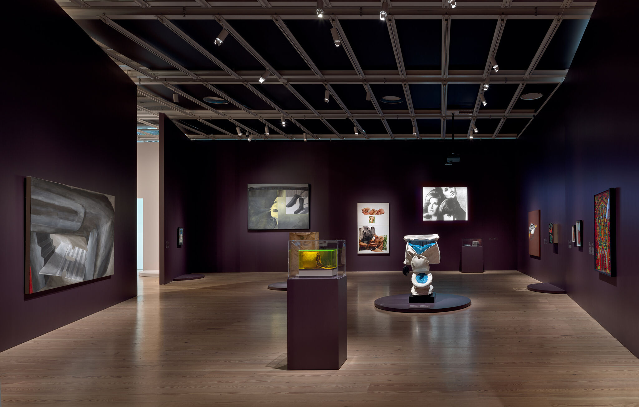 Gallery room with sculptures and paintings displayed on dark purple walls under track lighting.
