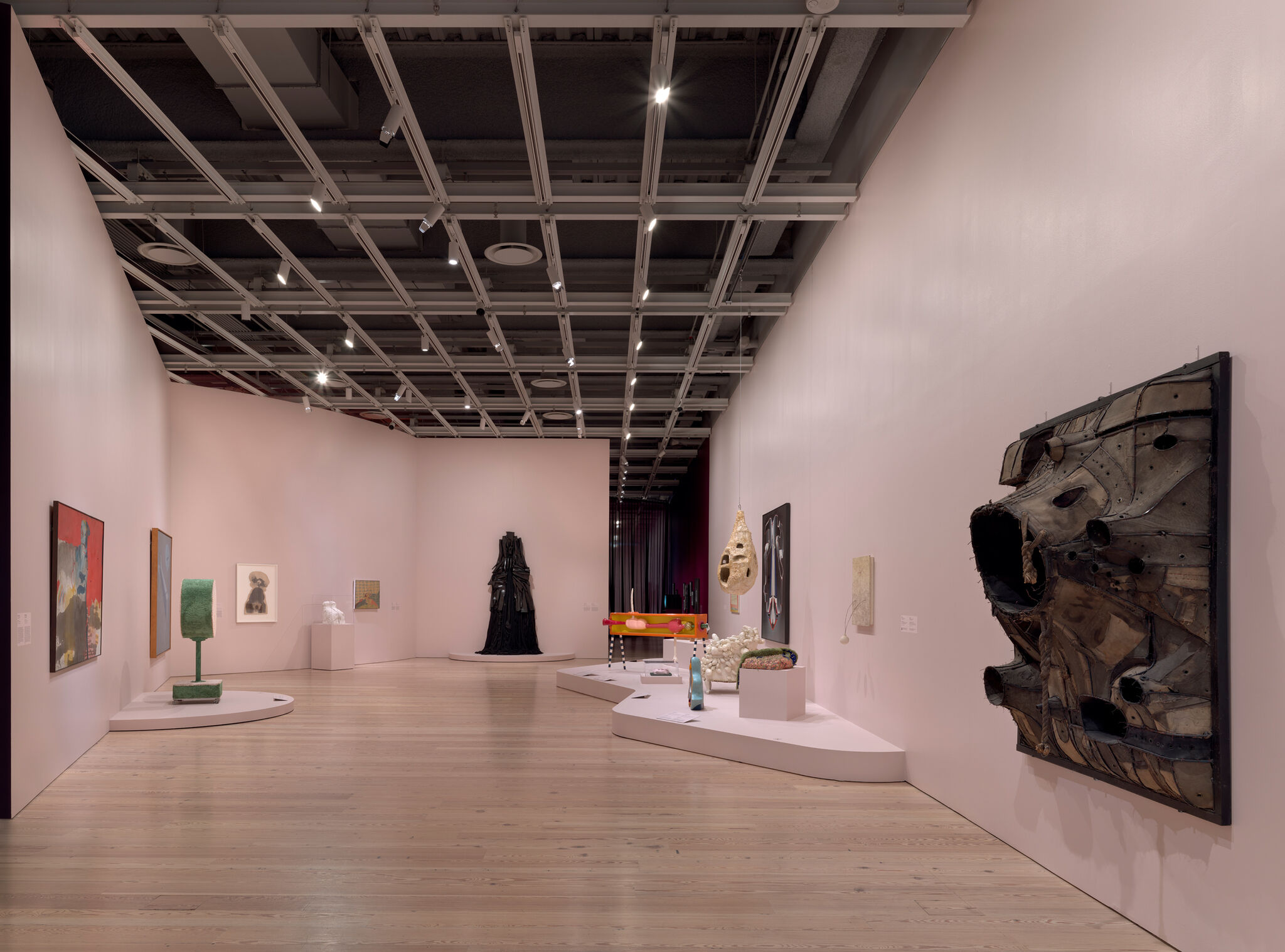 Contemporary sculptures and mixed-media artworks arranged along soft pink gallery walls and wooden floor.