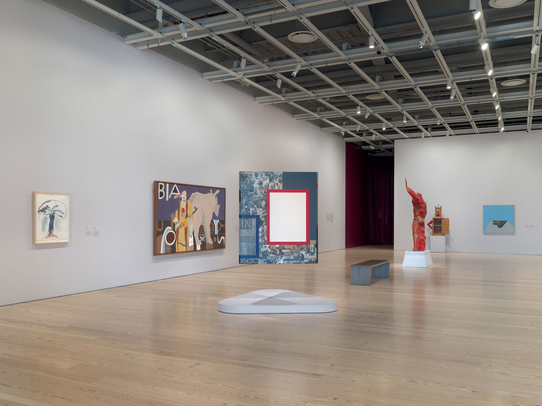 Contemporary gallery room displaying paintings, a red abstract sculpture raising an arm, and benches.