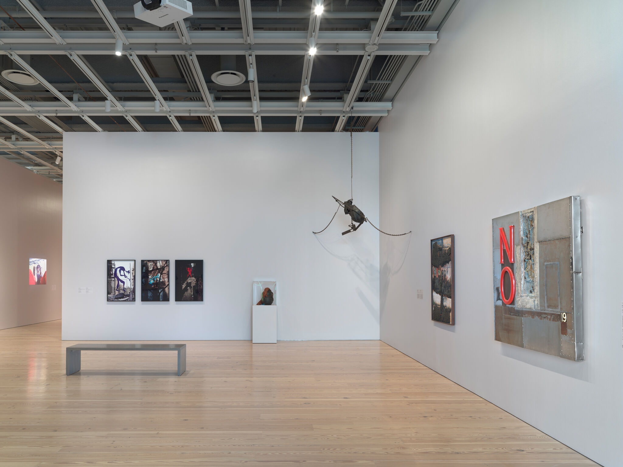 Gallery room displaying mixed-media artworks, including a large metal piece with red letters "NO".