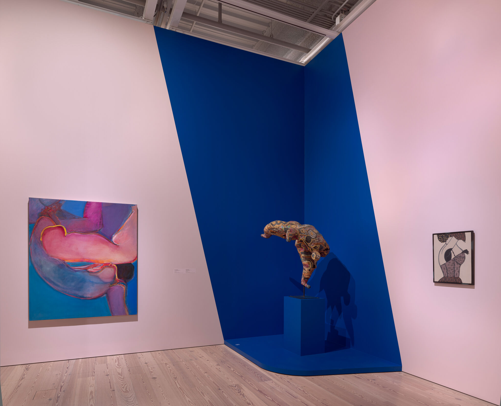 Sculpted patterned figure balancing on one leg in a bold blue corner, flanked by two paintings.