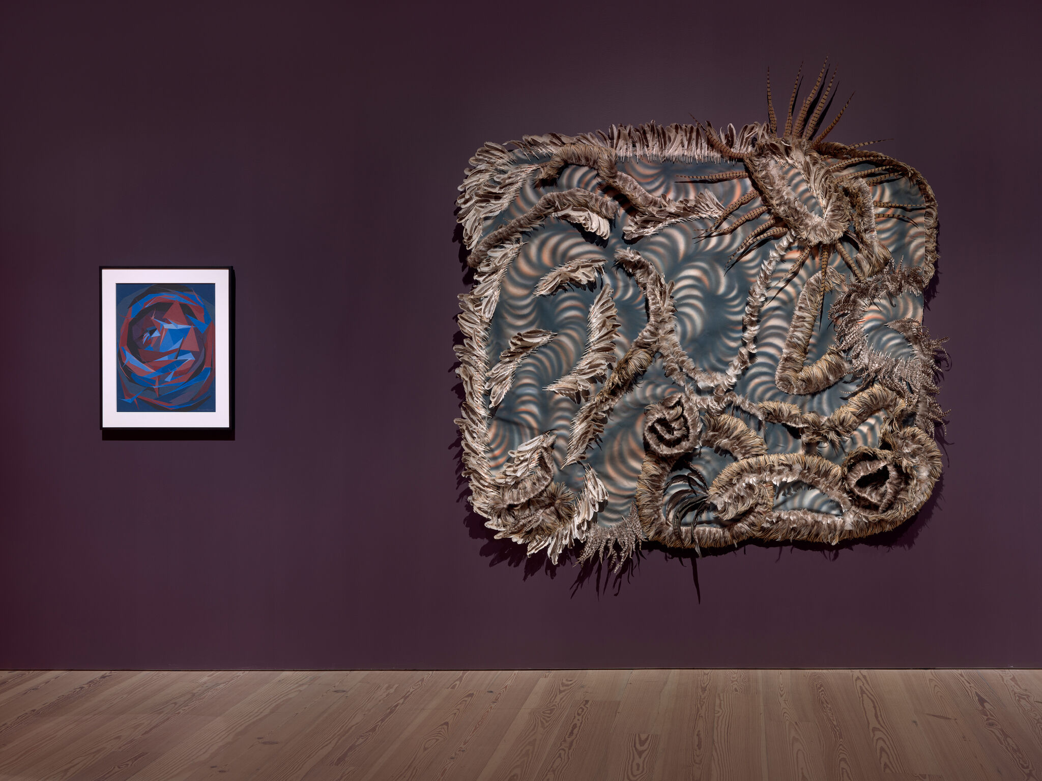 A framed blue-red abstract painting hangs beside a large feathered wall sculpture.