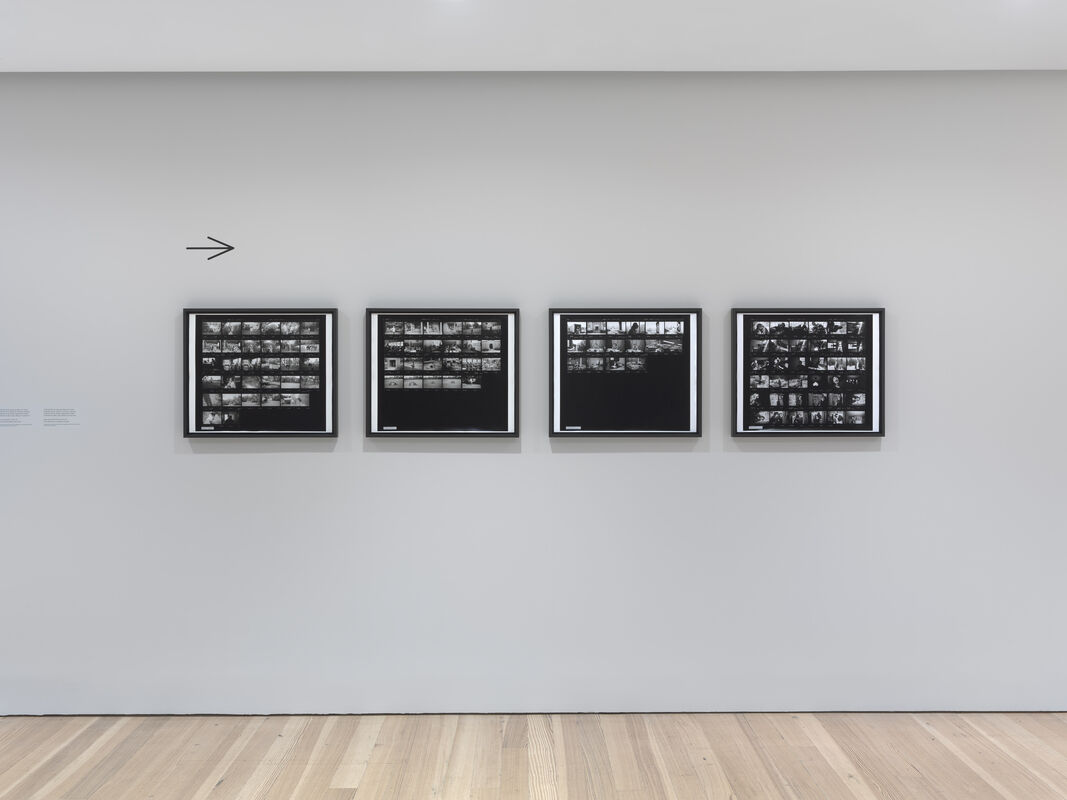 Four framed black-and-white contact sheet photographs hang in a row on a white gallery wall.