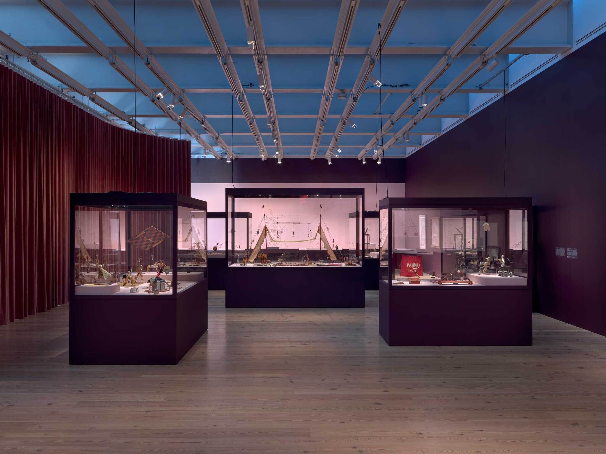 Museum gallery with three glass display cases showcasing small artifacts under track lighting.