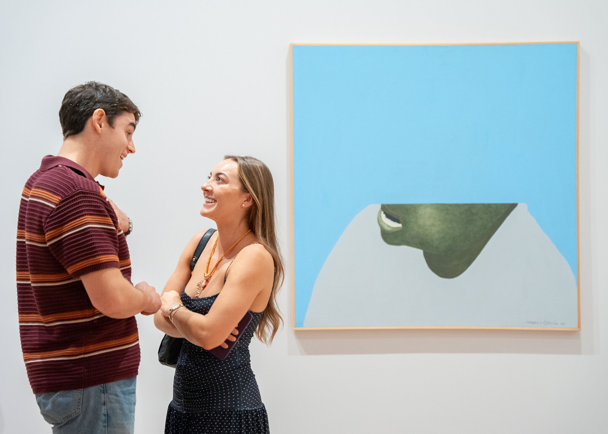 A smiling couple talk and laugh while standing in front of a large blue painting.