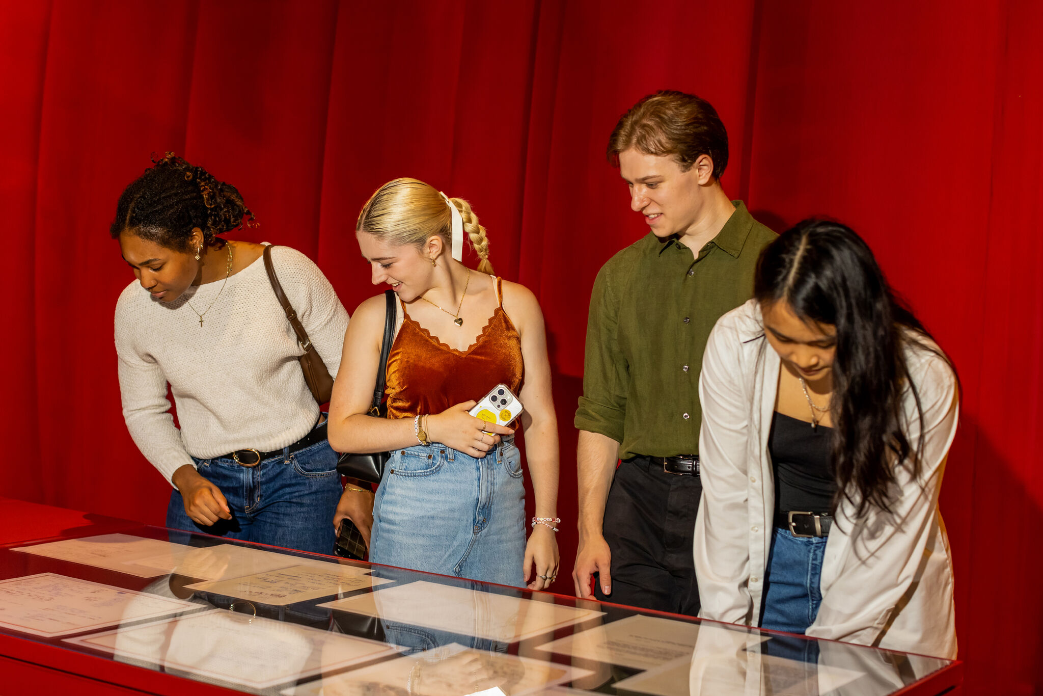 Four young adults lean over a display case and examine documents under glass.