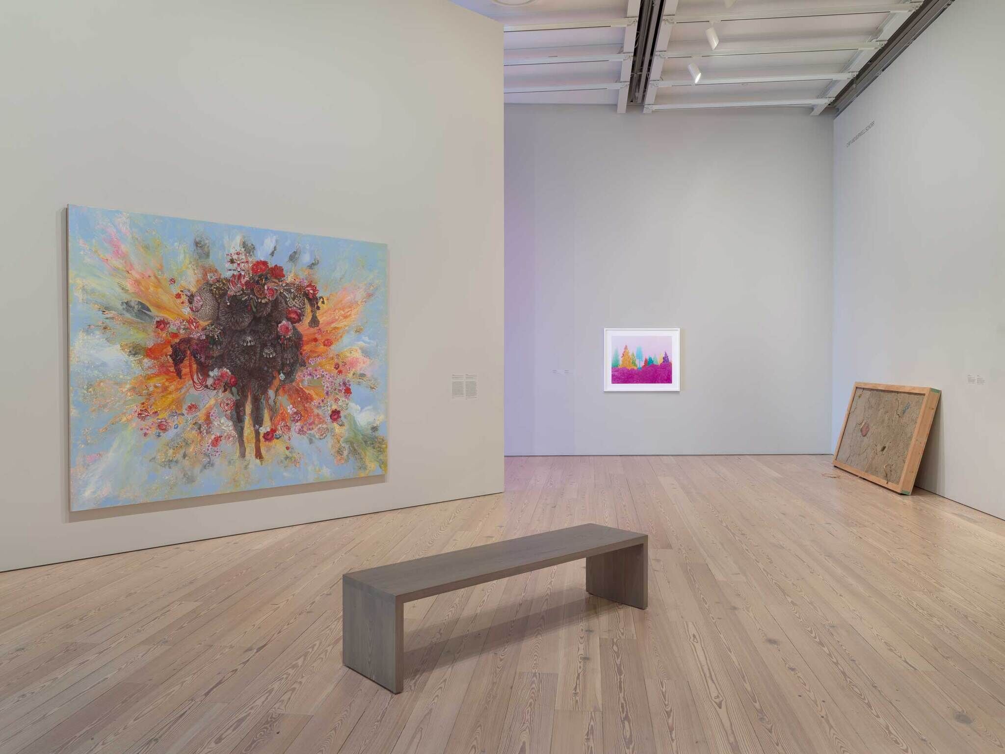 Bright abstract painting with floral explosion hangs on left wall of quiet gallery room.