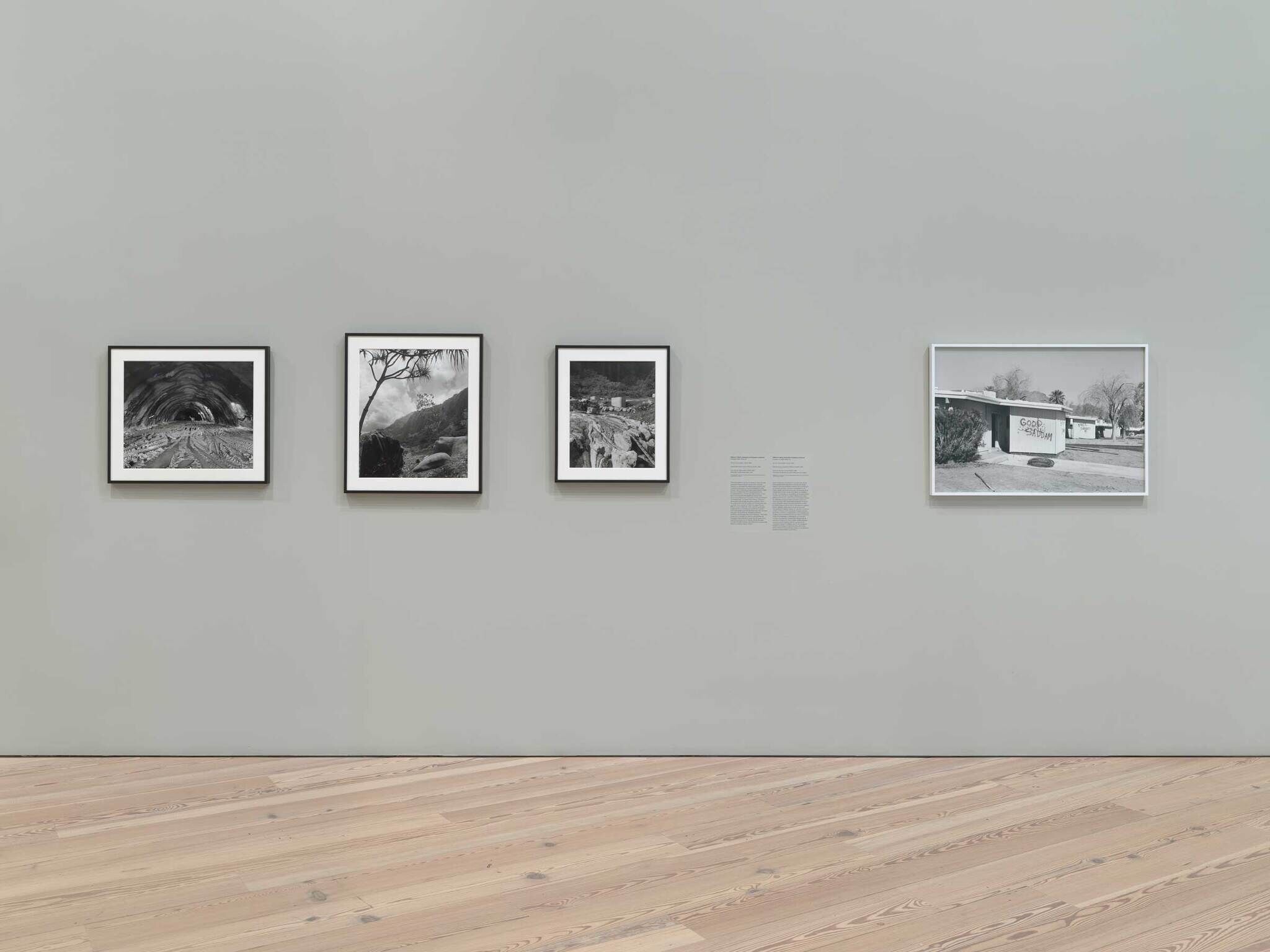 Four framed black-and-white photographs hang evenly spaced on a pale gallery wall above wooden flooring.