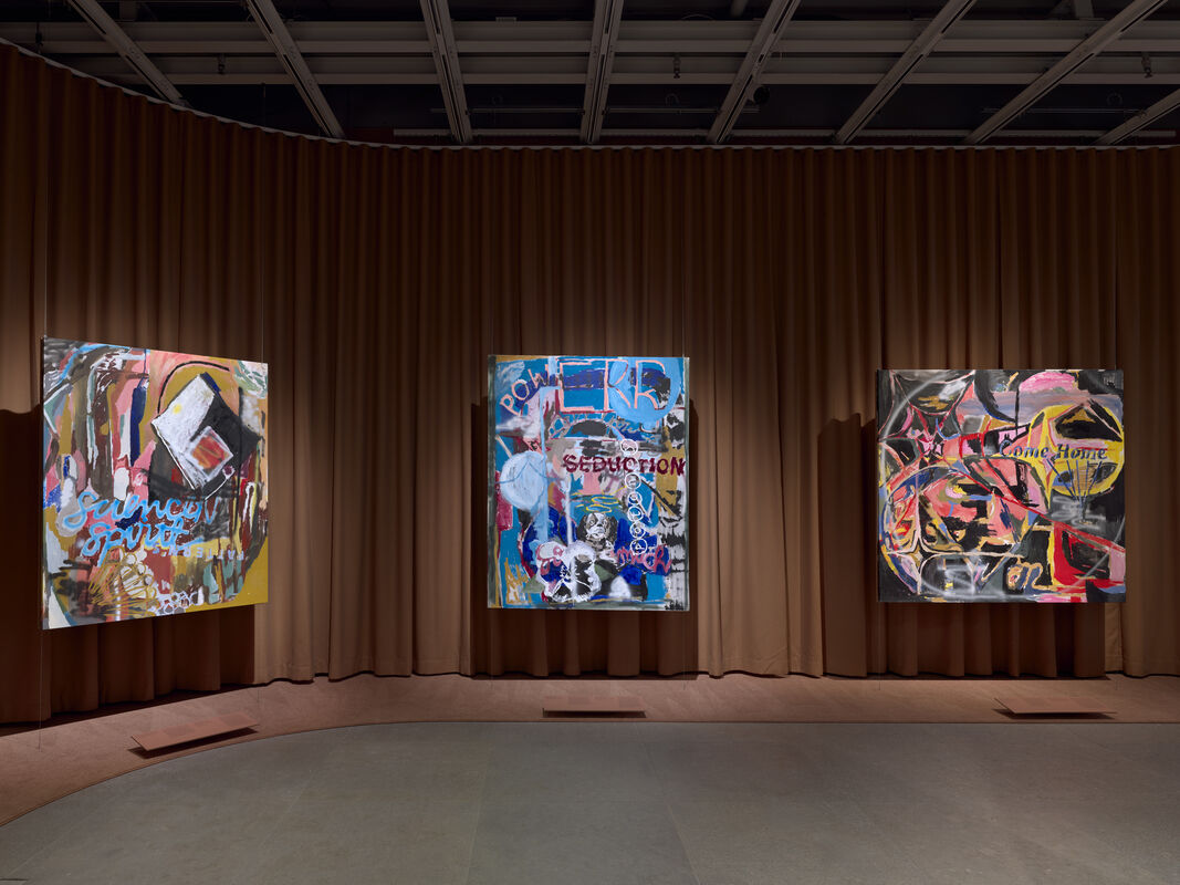 Three large colorful abstract paintings hang centered on a brown curtained gallery wall.