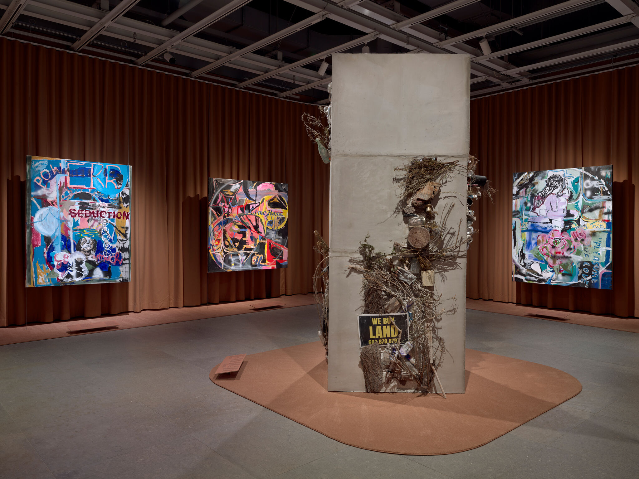 Concrete sculpture covered in branches, debris, and a "We Buy Land" sign standing in a gallery.