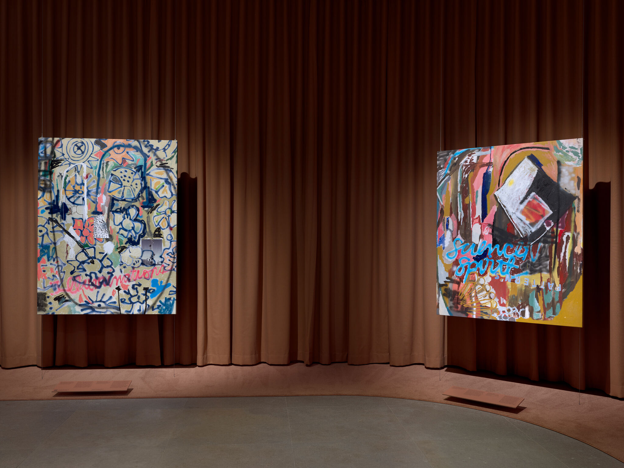Two large colorful abstract paintings hang suspended in a dim gallery space.