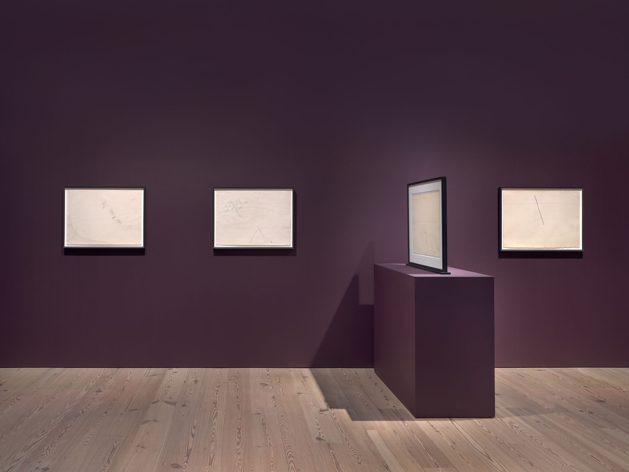 Four framed minimalist pencil drawings hang on a plum wall, one displayed on a pedestal.
