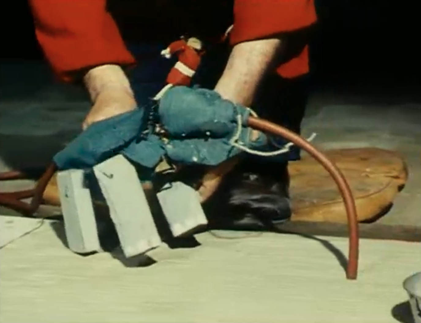 Person holds a homemade tool with concrete blocks and hoses near the floor.
