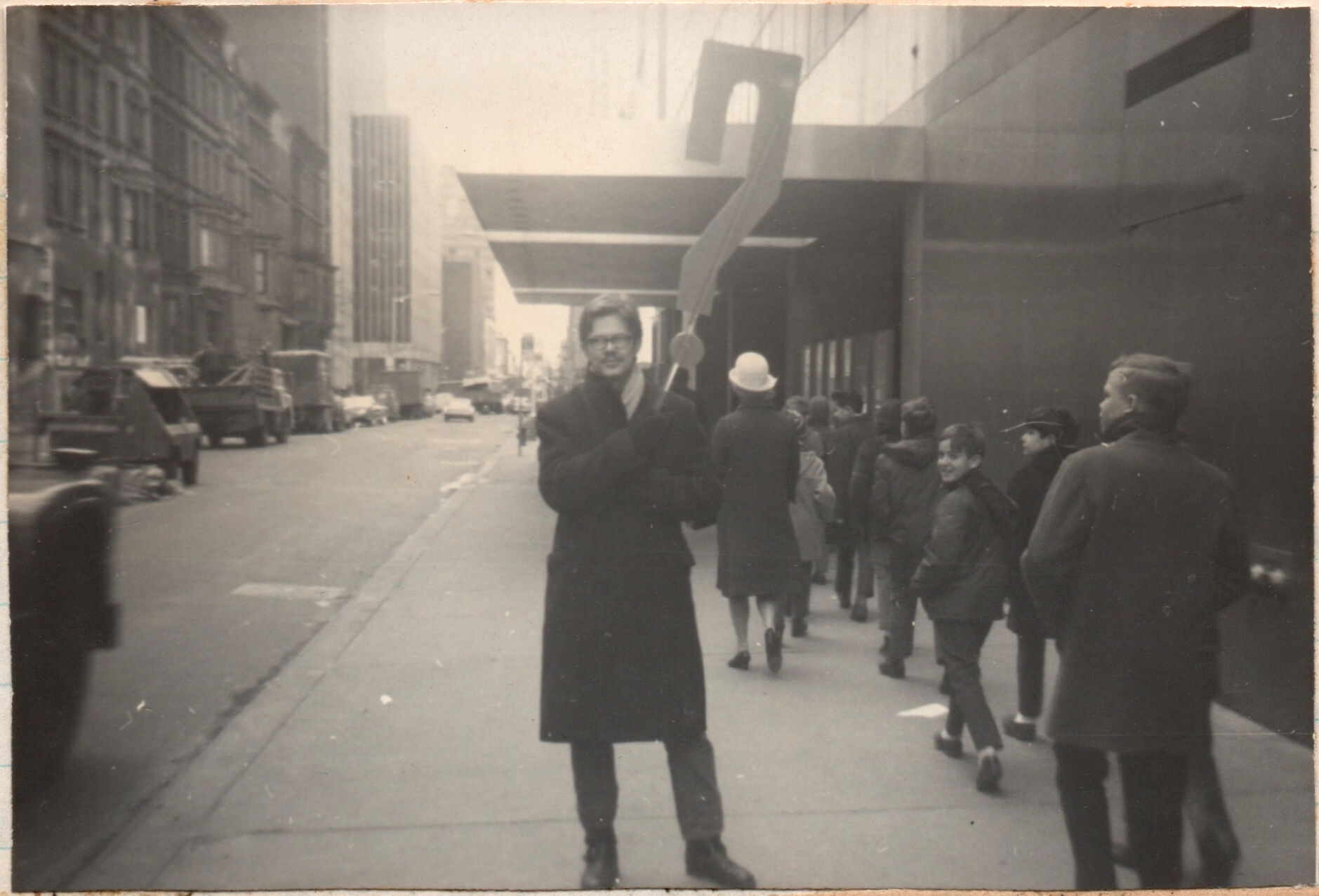 A 1968 black-and-white photograph of critic and curator Gene Swenson picketing outside the Museum of Modern Art, holding a giant question mark.