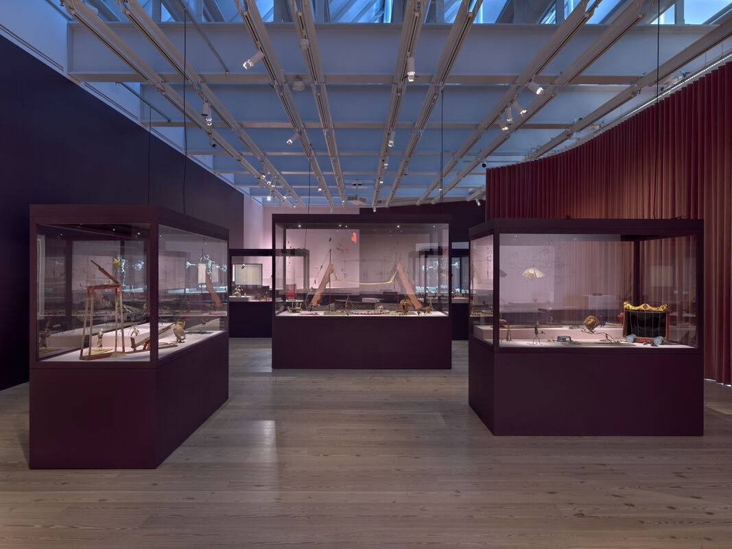 Museum gallery with glass display cases showcasing small historical artifacts under skylight lighting.