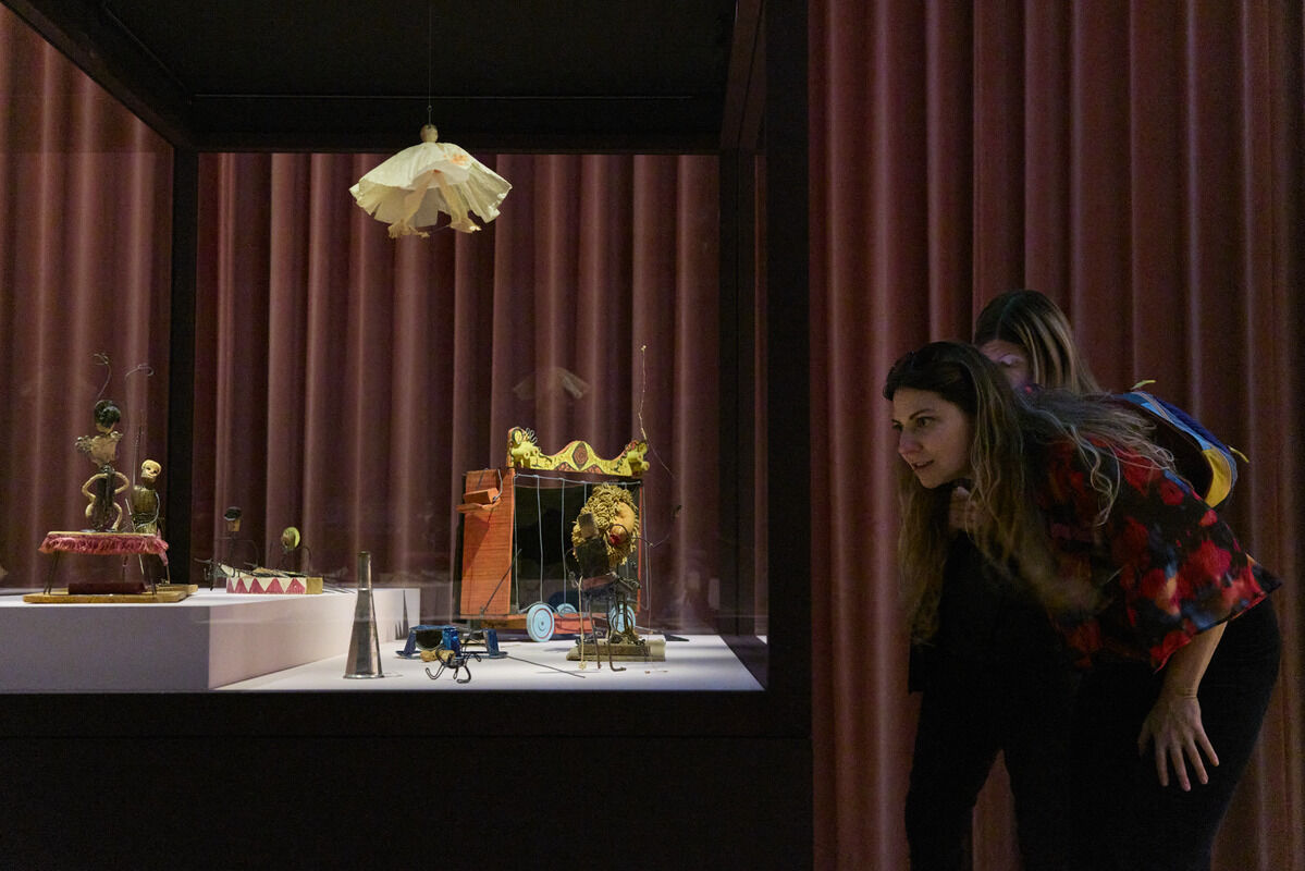 Two women lean forward to closely examine a display of vintage mechanical toys behind glass.